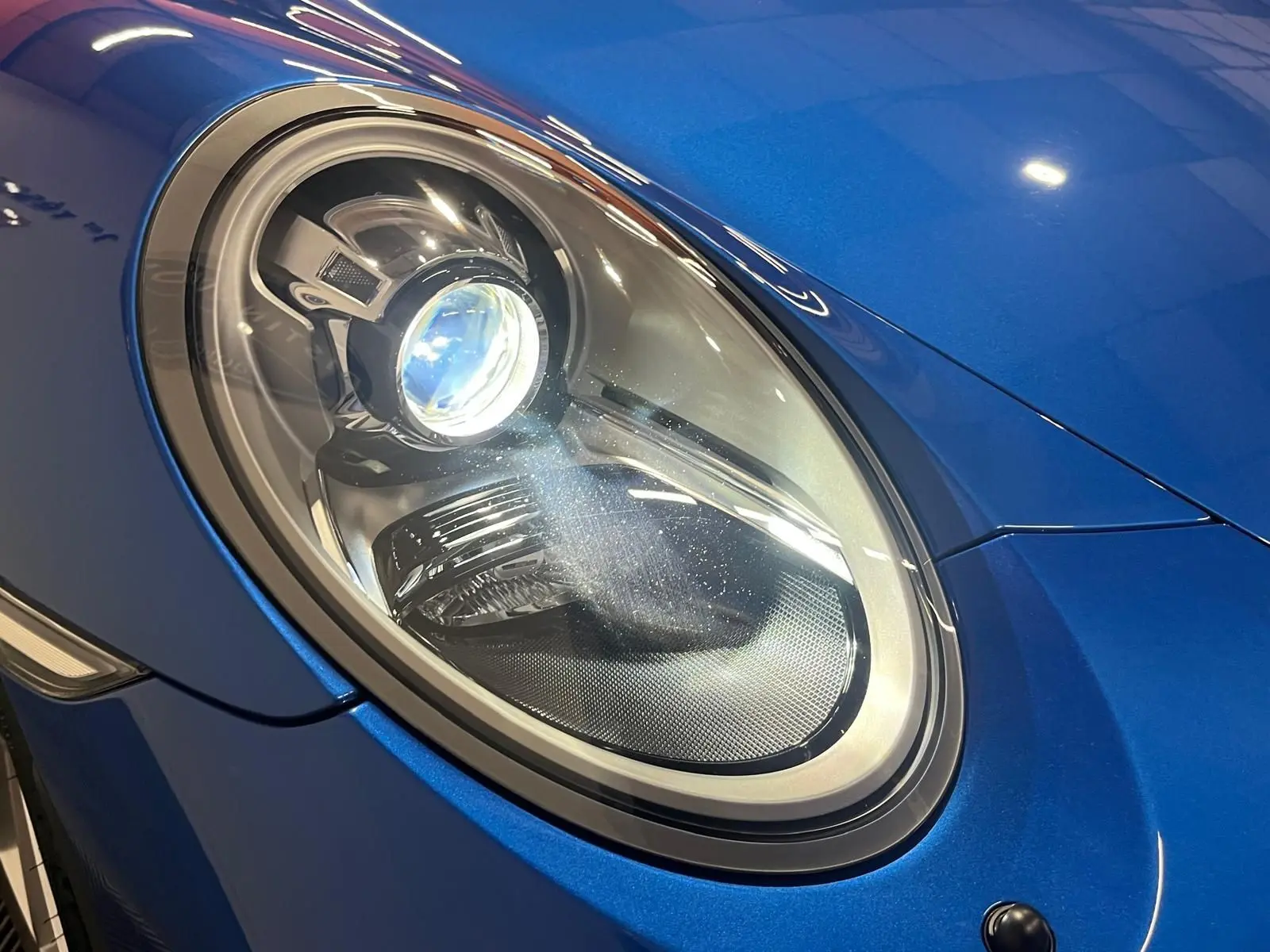 Gros plan sur le phare avant gauche d'une Porsche 911 GT3 bleu saphir brillant, soulignant ses détails modernes.