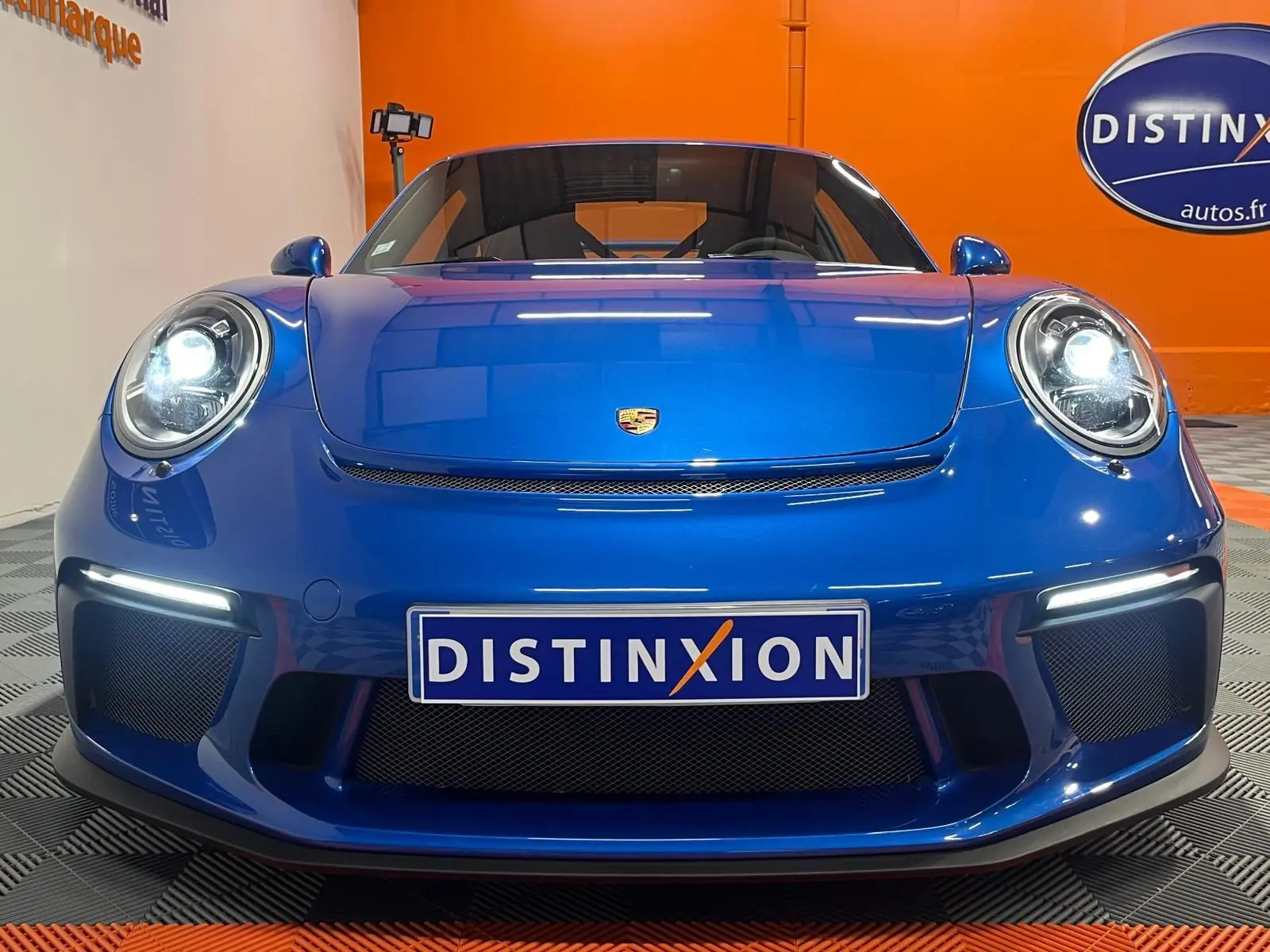 Vue frontale rapprochée de la Porsche 911 GT3 bleu saphir avec phares allumés et plaque Distinxion.