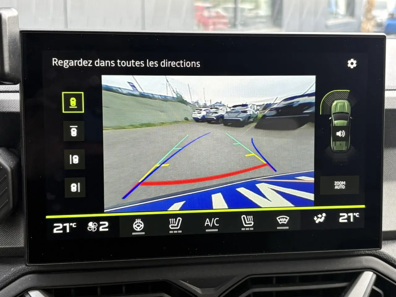 Écran tactile affichant la caméra multivues du Dacia Bigster blanc banquise en marche arrière avec lignes de guidage colorées.