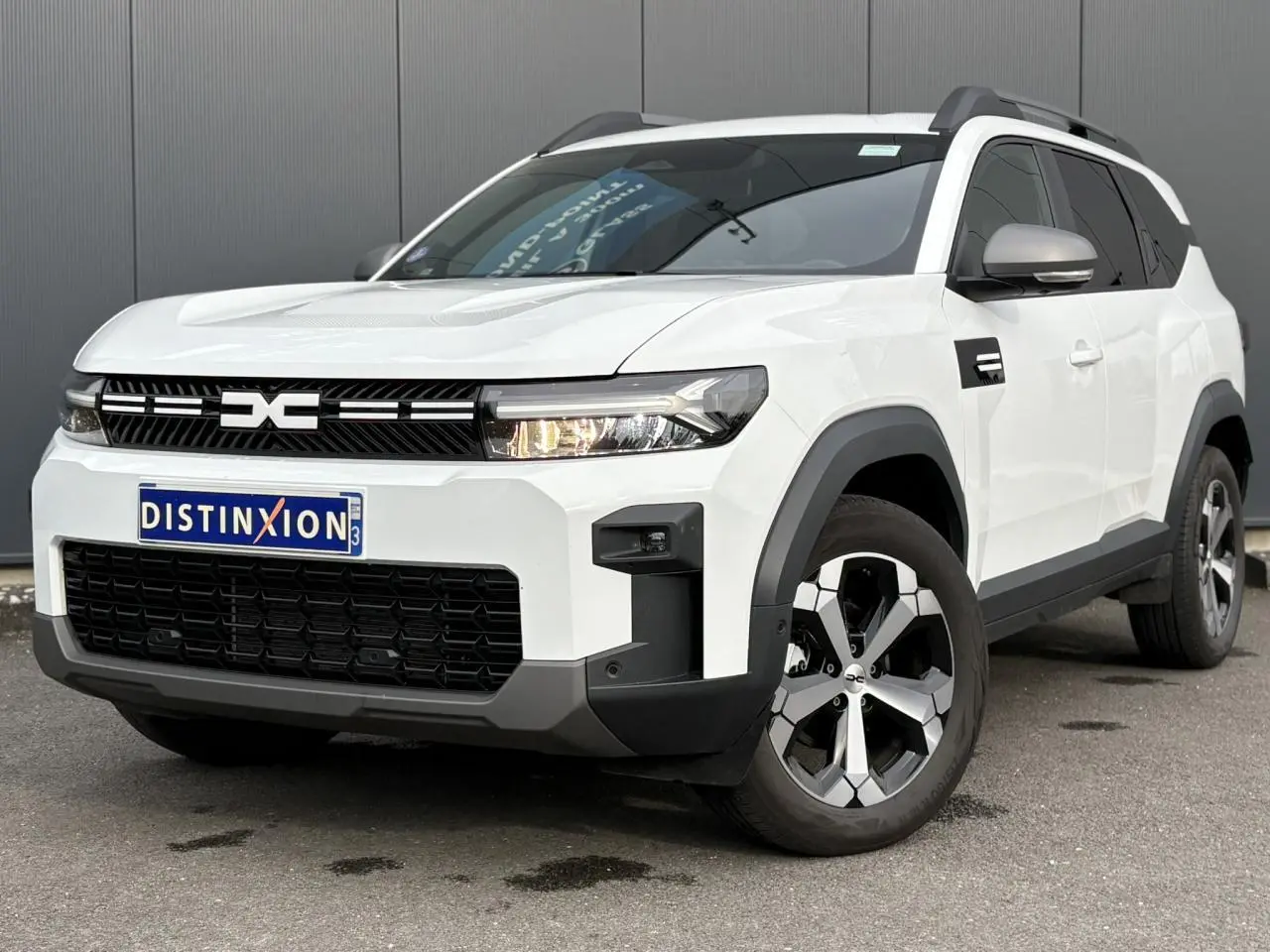 Vue 3/4 avant droit du Dacia Bigster blanc Banquise avec jantes alliage et barres de toit gris mégalithe.