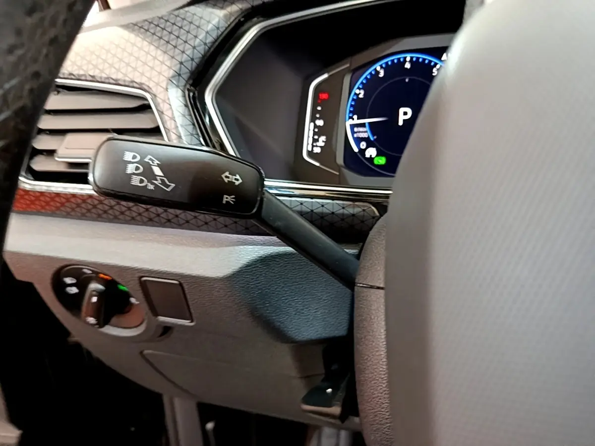 Détail du commodo gauche et tableau de bord numérique bleu du Volkswagen T-Cross 1.0 TSI noir, vue intérieure côté conducteur.