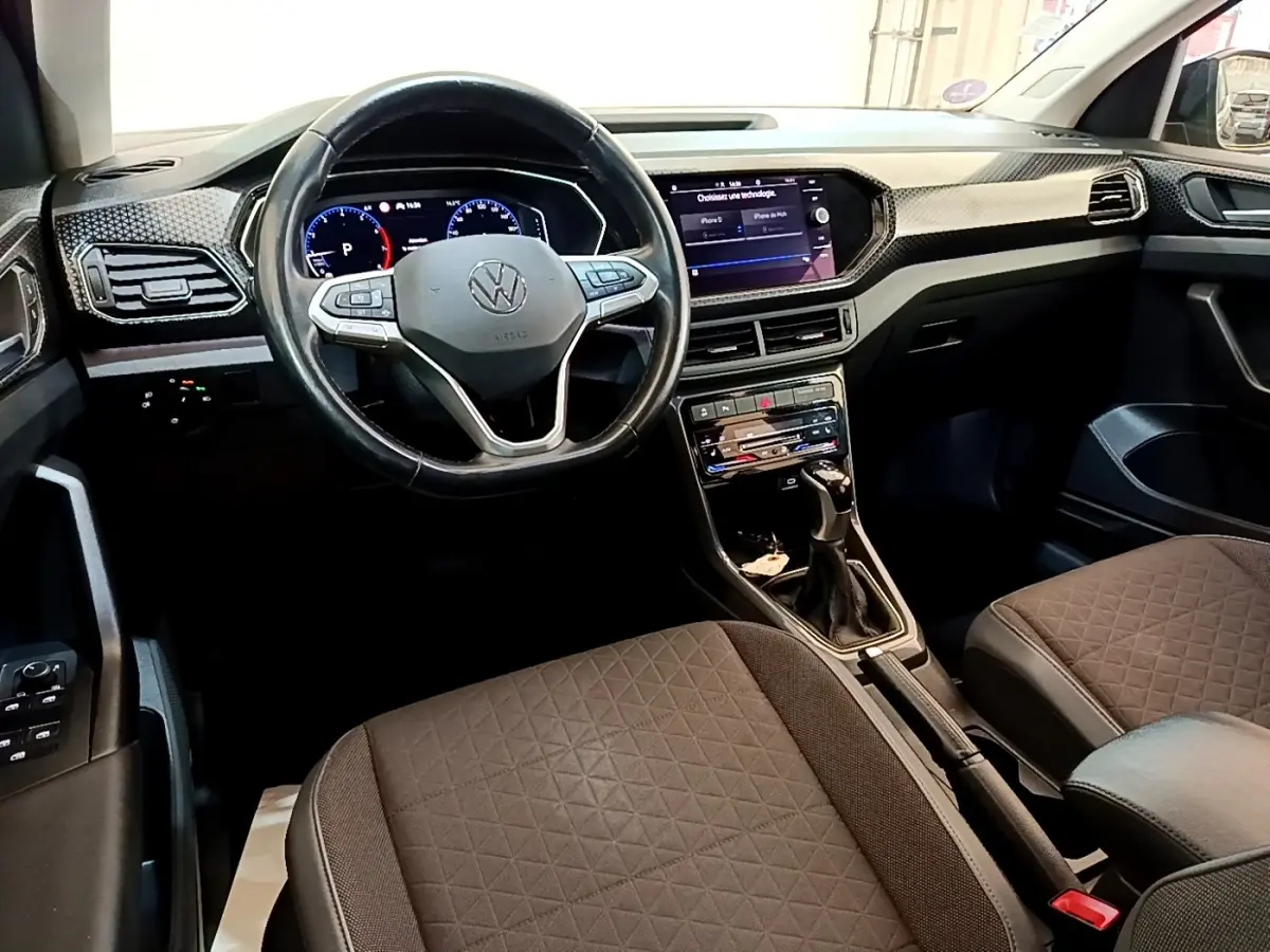 Vue intérieure avant du Volkswagen T-Cross 2022, montrant le volant multifonctions, tableau de bord digital et sièges tissu marron.