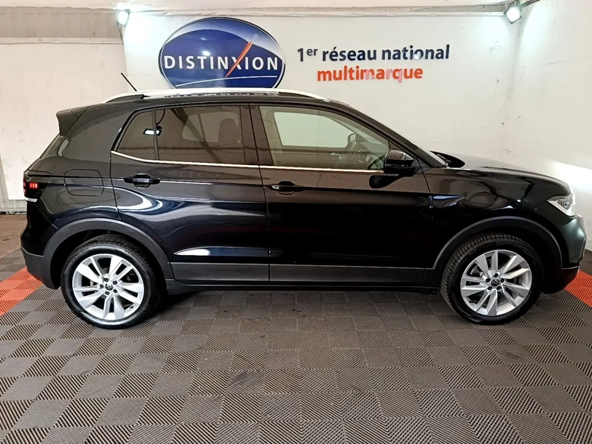 Profil droit d’un Volkswagen T-Cross noir 2022, avec jantes alliage et vitres teintées, sur fond intérieur showroom.