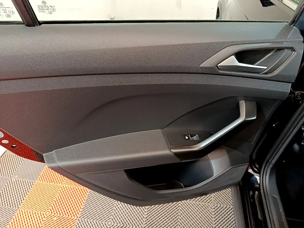 Vue rapprochée de la porte avant gauche noire du Volkswagen T-Cross 2022, avec poignée et commande de vitre électrique.