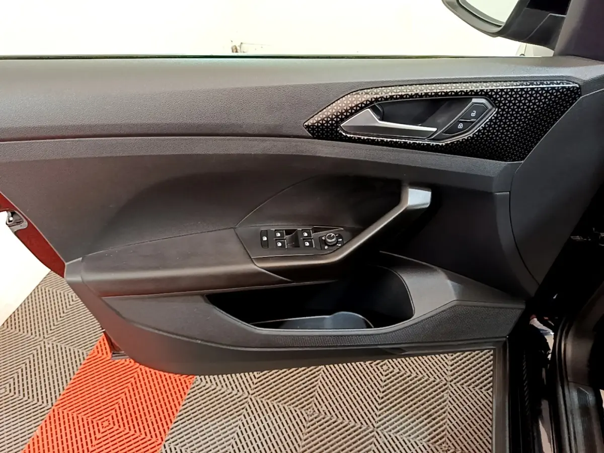 Vue intérieure du panneau de porte avant gauche noir du Volkswagen T-Cross avec commandes électriques et poignée design texturée.