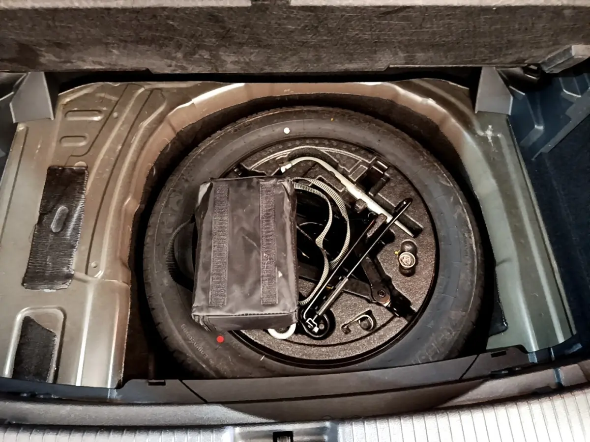 Vue plongeante sur la roue de secours et outils dans le coffre du Volkswagen T-Cross noir, version 2022.