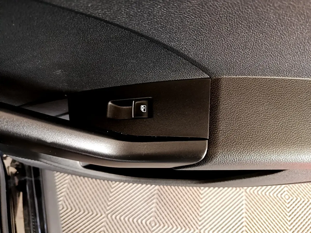 Gros plan sur la commande de verrouillage de porte côté conducteur d’un Volkswagen T-Cross noir, intérieur sombre.