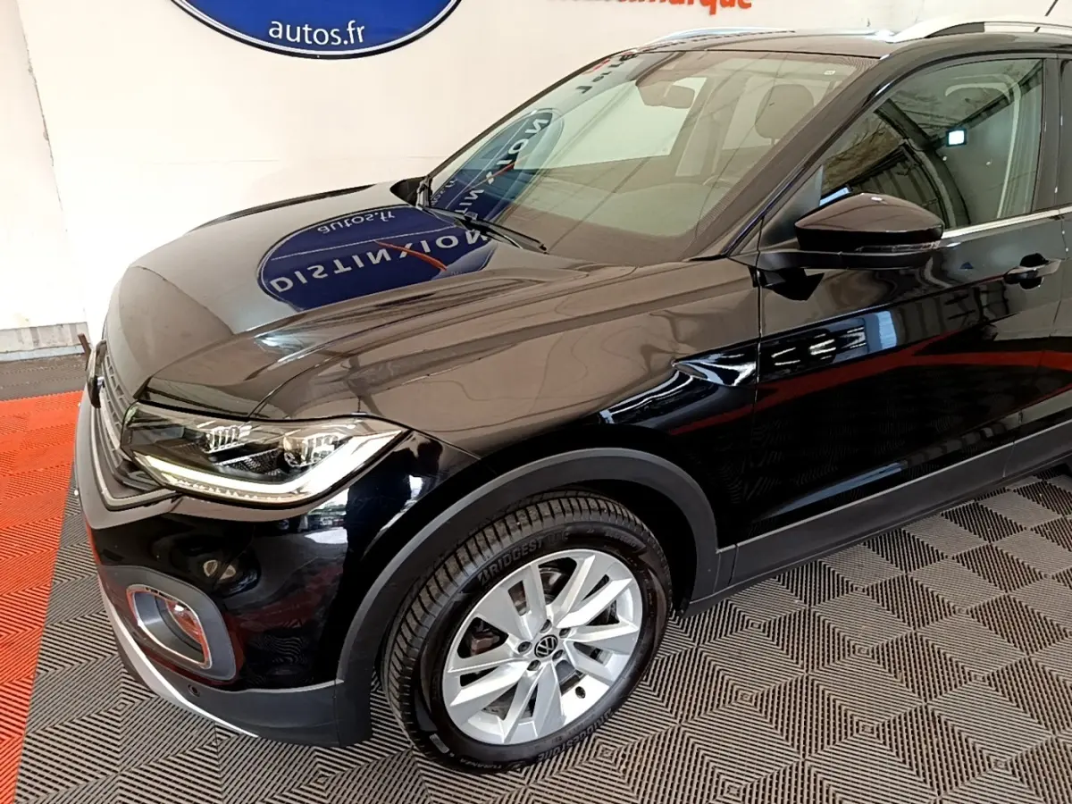 Vue 3/4 avant droit d'un Volkswagen T-Cross noir brillant, mettant en valeur ses phares LED et jantes alliage.