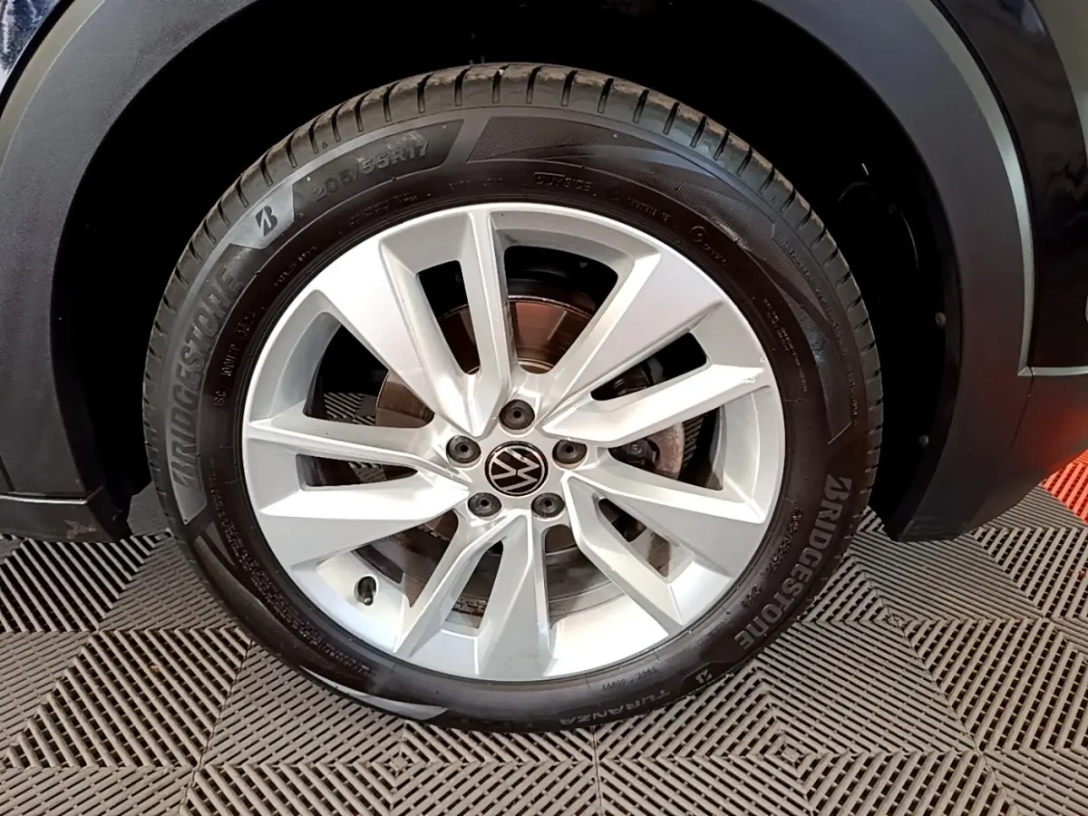 Gros plan sur la roue avant droite du Volkswagen T-Cross noir, jante alliage argentée avec logo VW central.