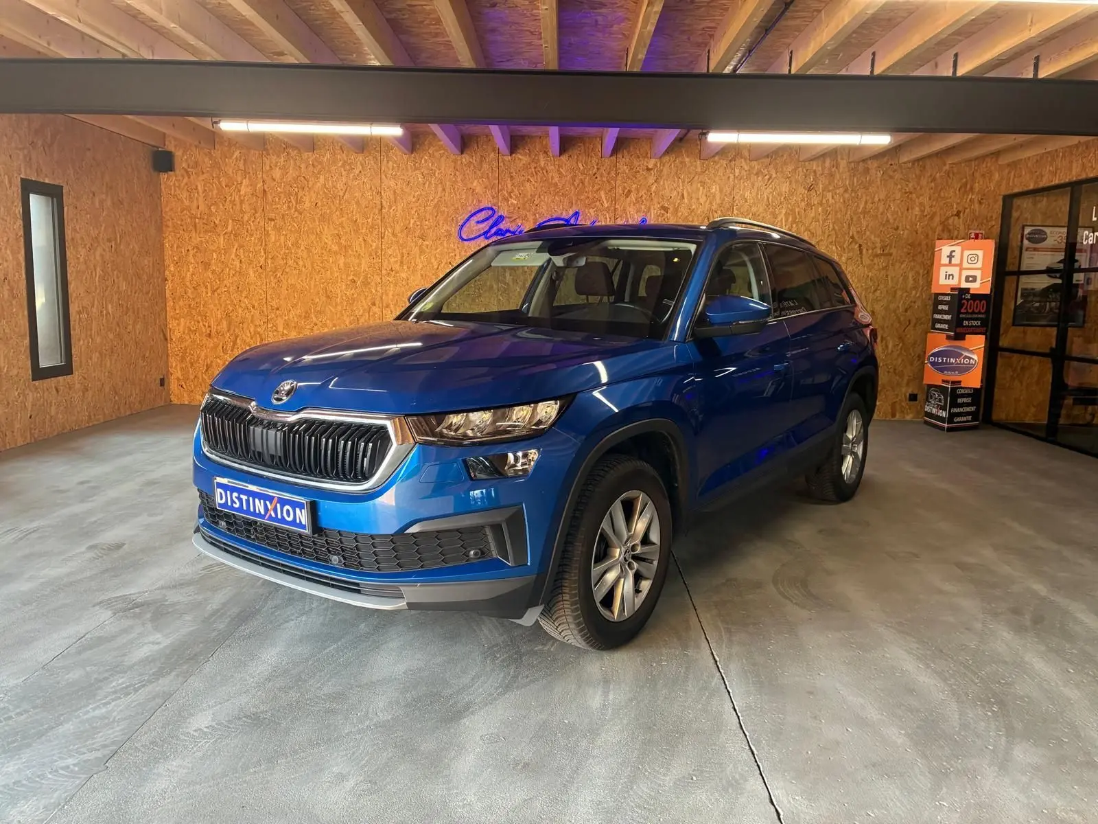 SUV SKODA KODIAQ bleu 2023 en 3/4 avant droit, avec calandre noire et jantes argentées, dans un showroom intérieur.