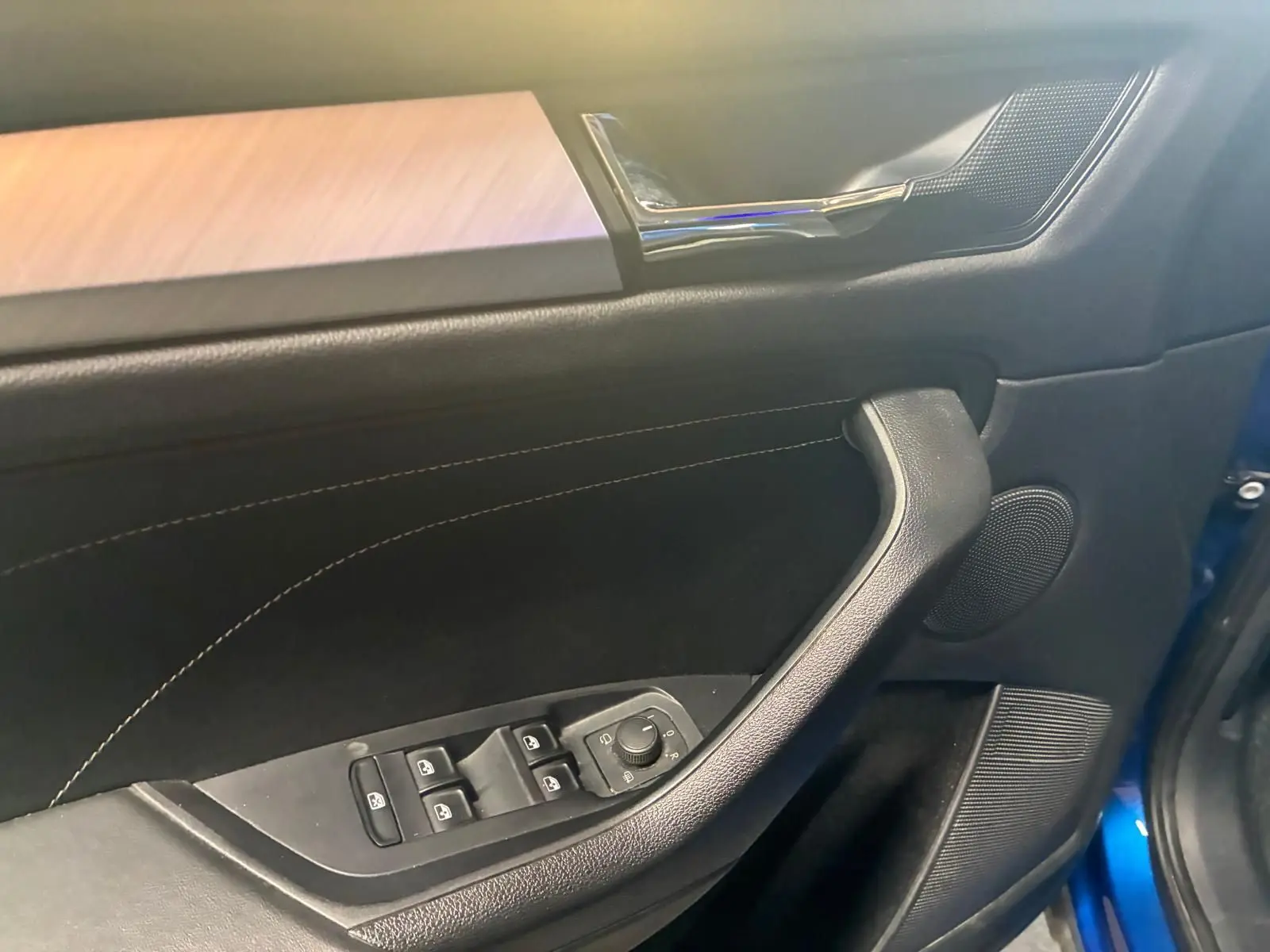Détail de la porte avant gauche du Skoda Kodiaq bleu 2023, montrant les commandes des vitres et le revêtement noir avec surpiqûres.