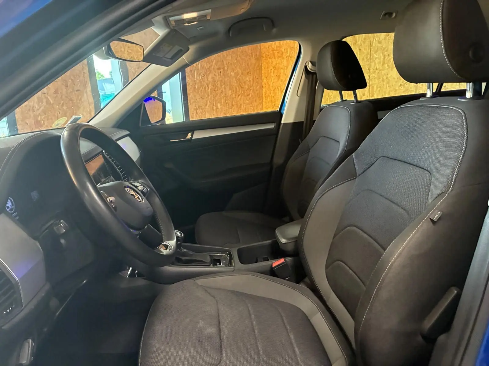 Vue intérieure côté conducteur du Skoda Kodiaq bleu 2023, mettant en valeur les sièges noirs en tissu et le volant multifonction.