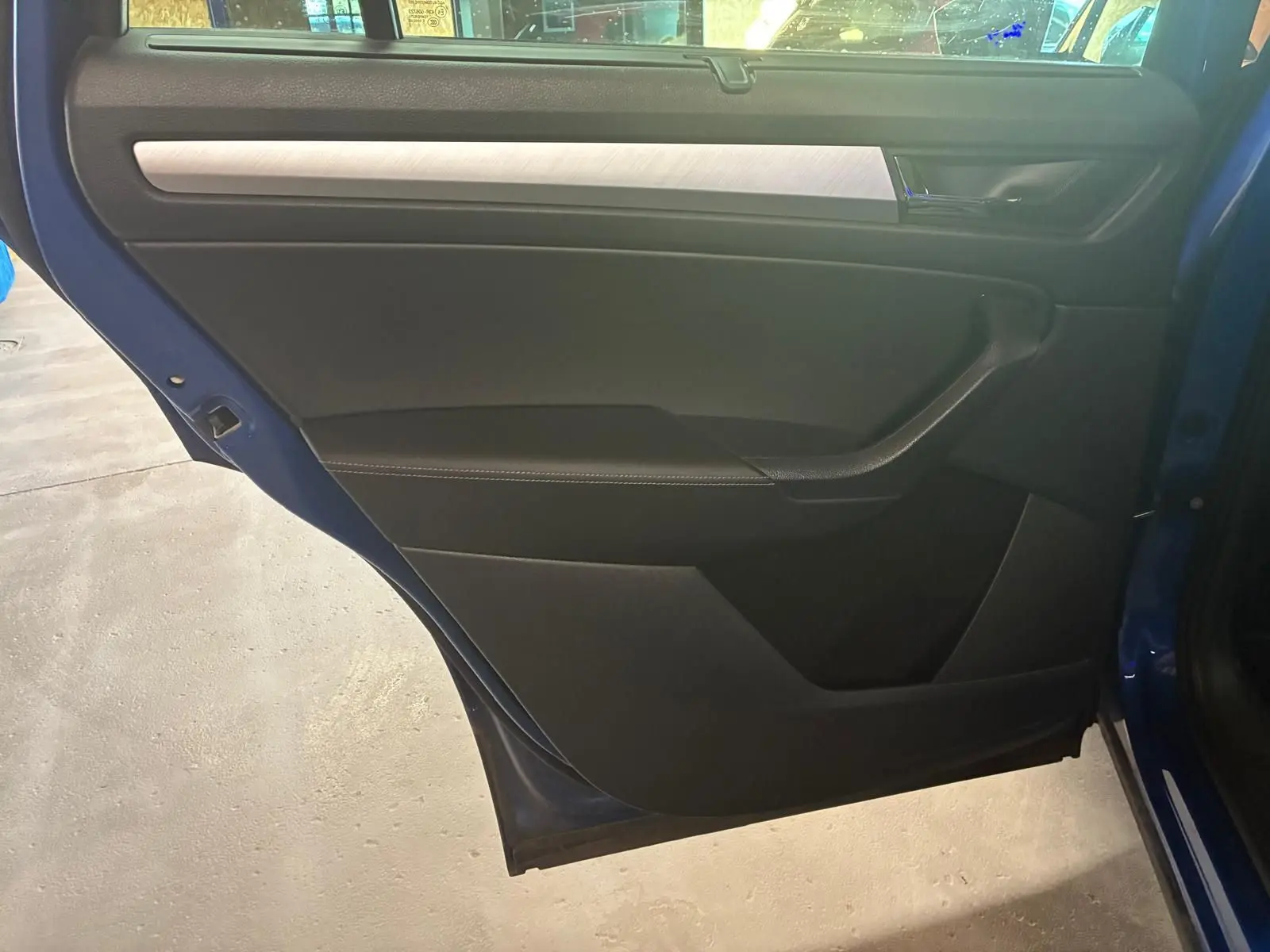 Vue intérieure de la porte arrière gauche d’un Skoda Kodiaq bleu 2023 avec garniture noire et insert argenté.