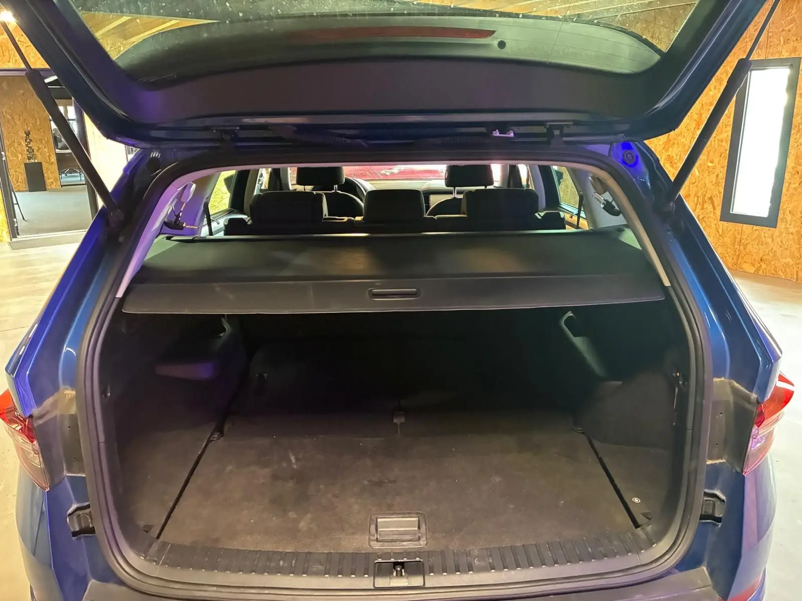 Coffre ouvert d’un Skoda Kodiaq bleu 2023, vue arrière montrant l’espace de chargement avec cache-bagages déployé.