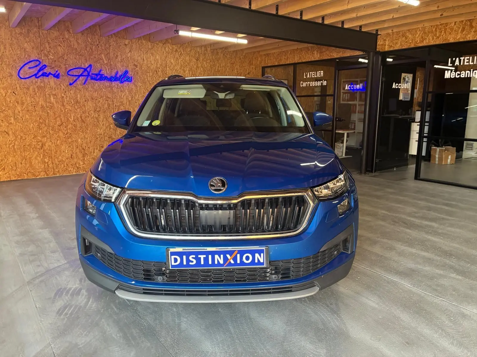 Vue avant d'un Skoda Kodiaq bleu 2023, mettant en valeur la calandre noire et les phares LED dans un showroom.