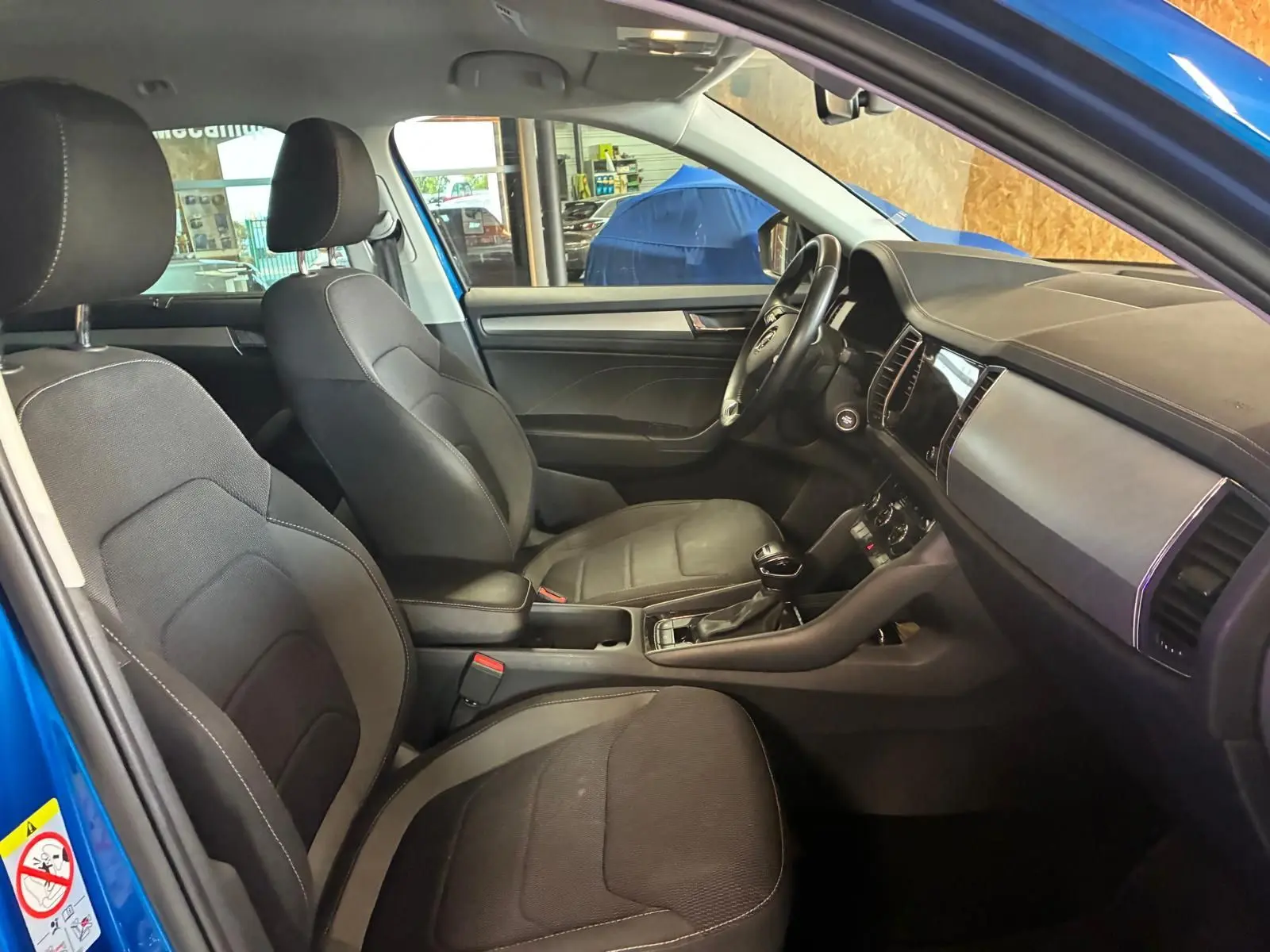 Intérieur du Skoda Kodiaq 2023 bleu, vue côté gauche montrant les sièges tissu noirs et le tableau de bord moderne.