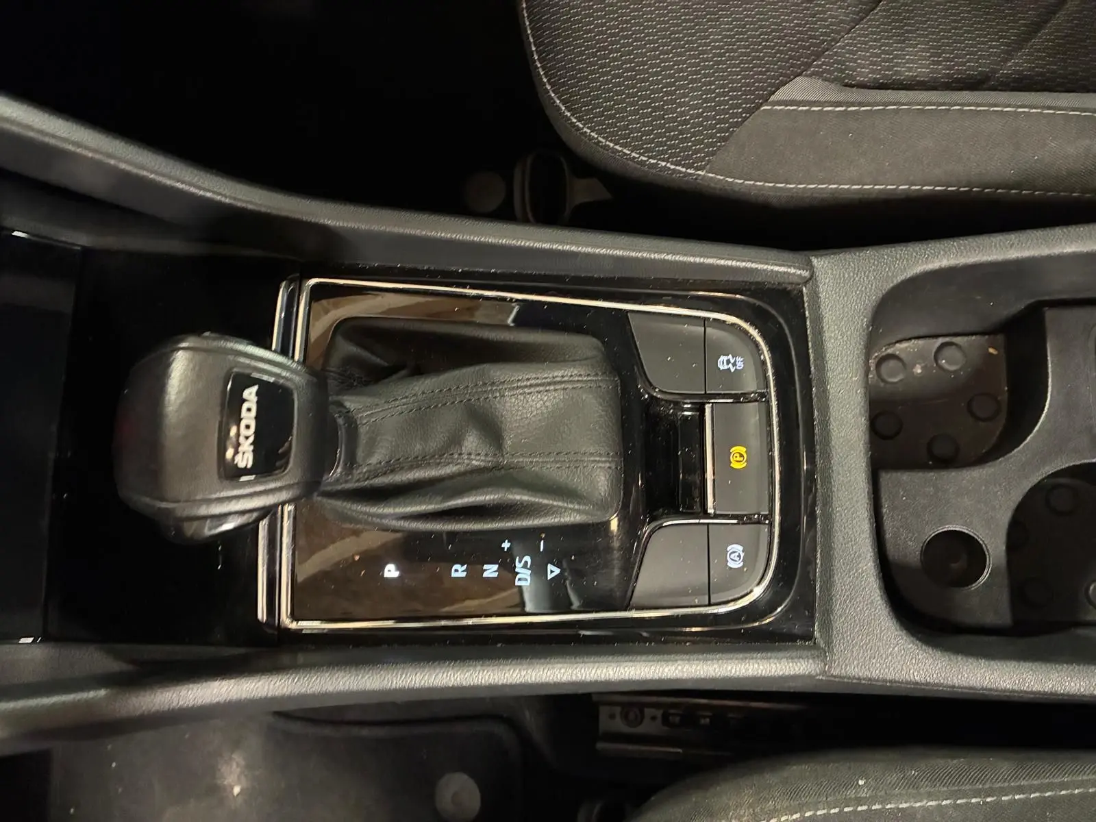 Vue rapprochée du levier de vitesses automatique noir marqué SKODA, entouré de boutons de commande, intérieur tissu noir.