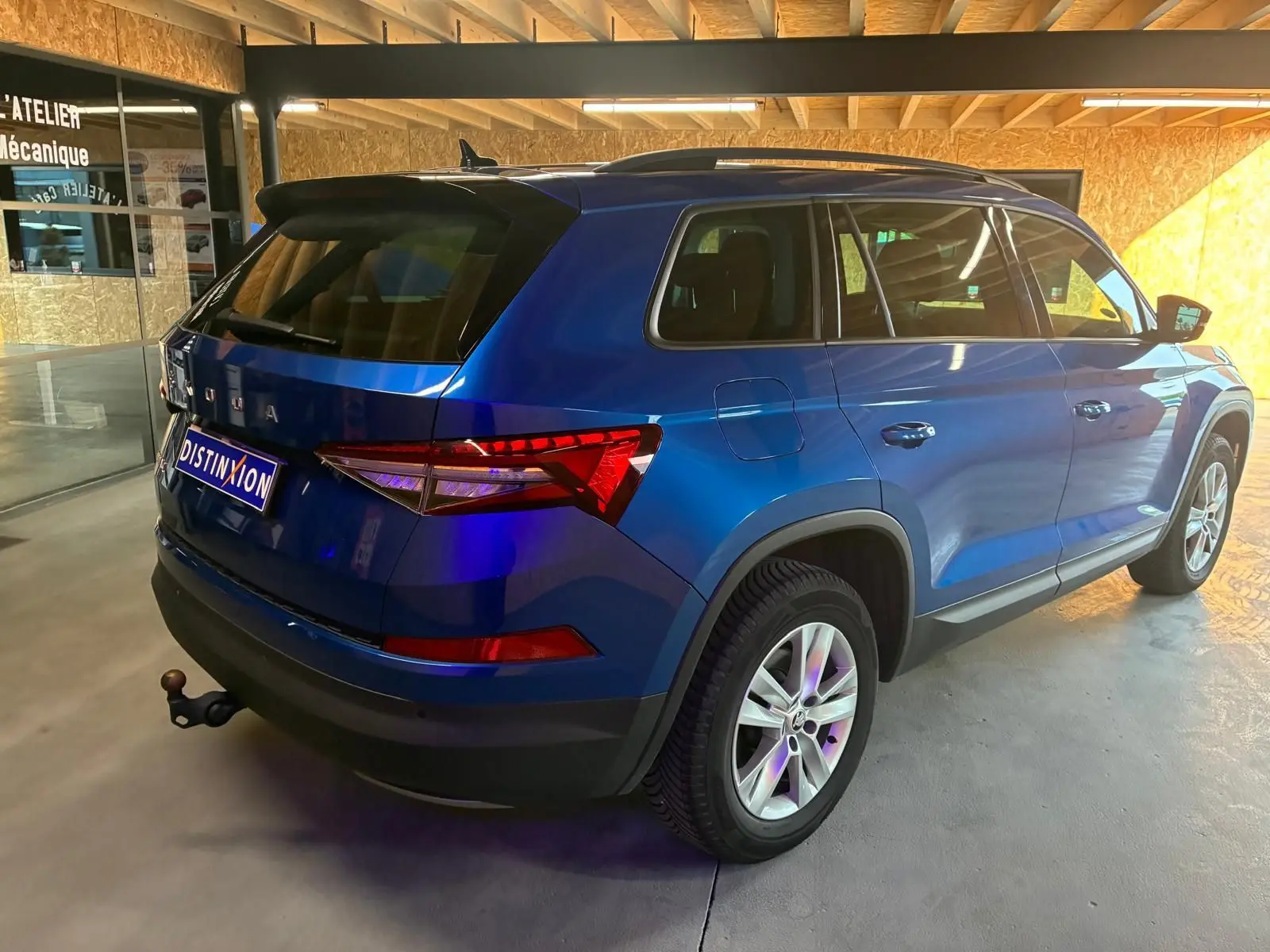 Vue 3/4 arrière droite d'un Skoda Kodiaq bleu 2023 avec attelage et vitres teintées, stationné en intérieur.