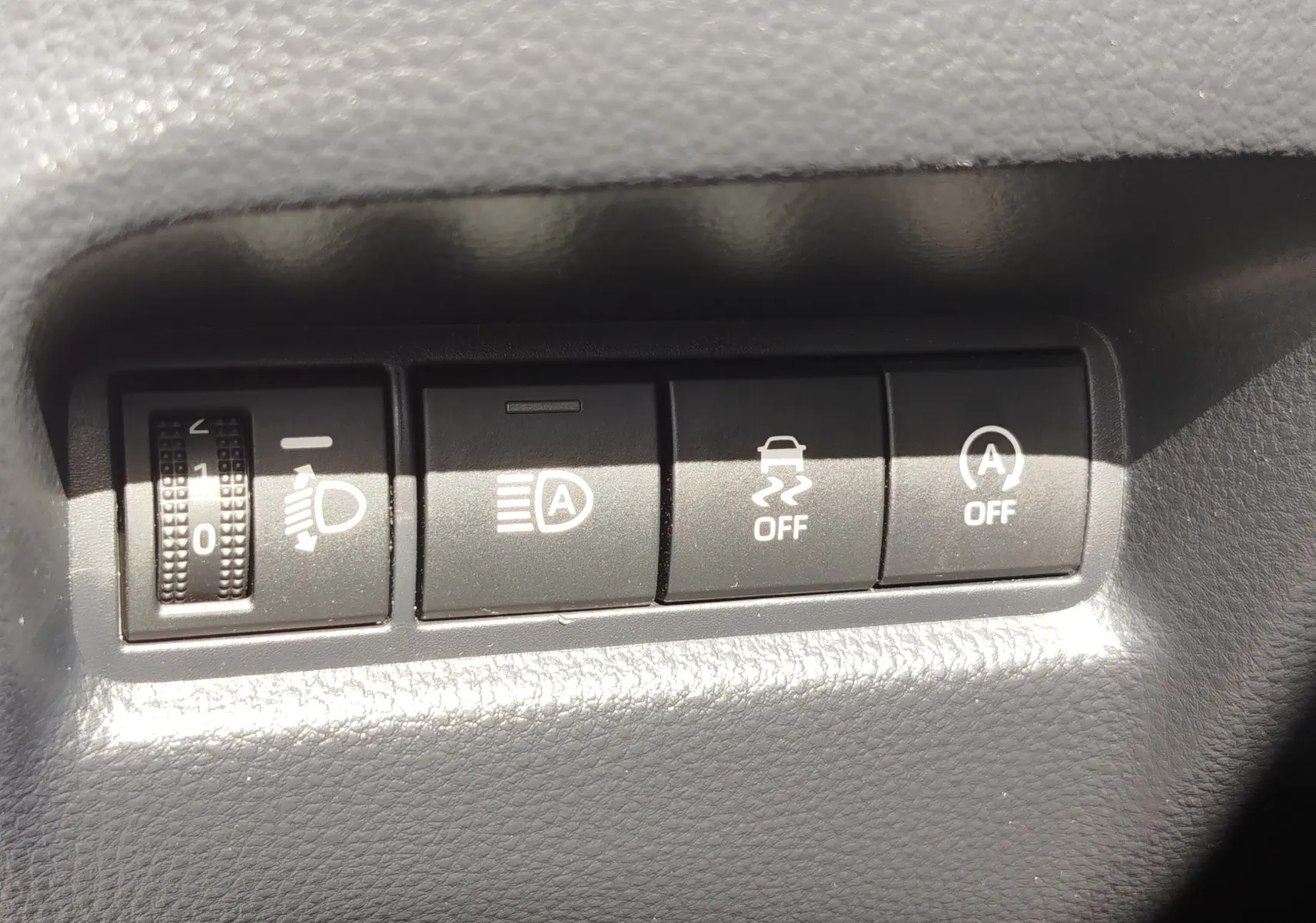 Gros plan sur les commandes de réglage des phares et des aides à la conduite dans une Toyota Aygo X blanche.