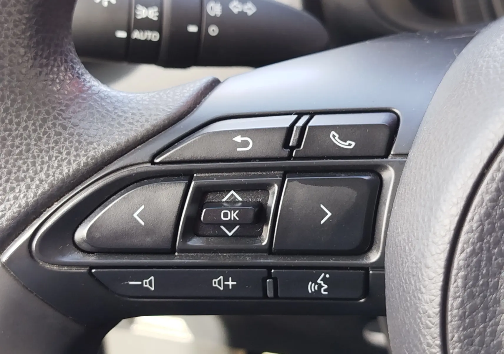 Gros plan sur les commandes noires du volant côté gauche de la Toyota Aygo X blanche, avec boutons de navigation et appel.