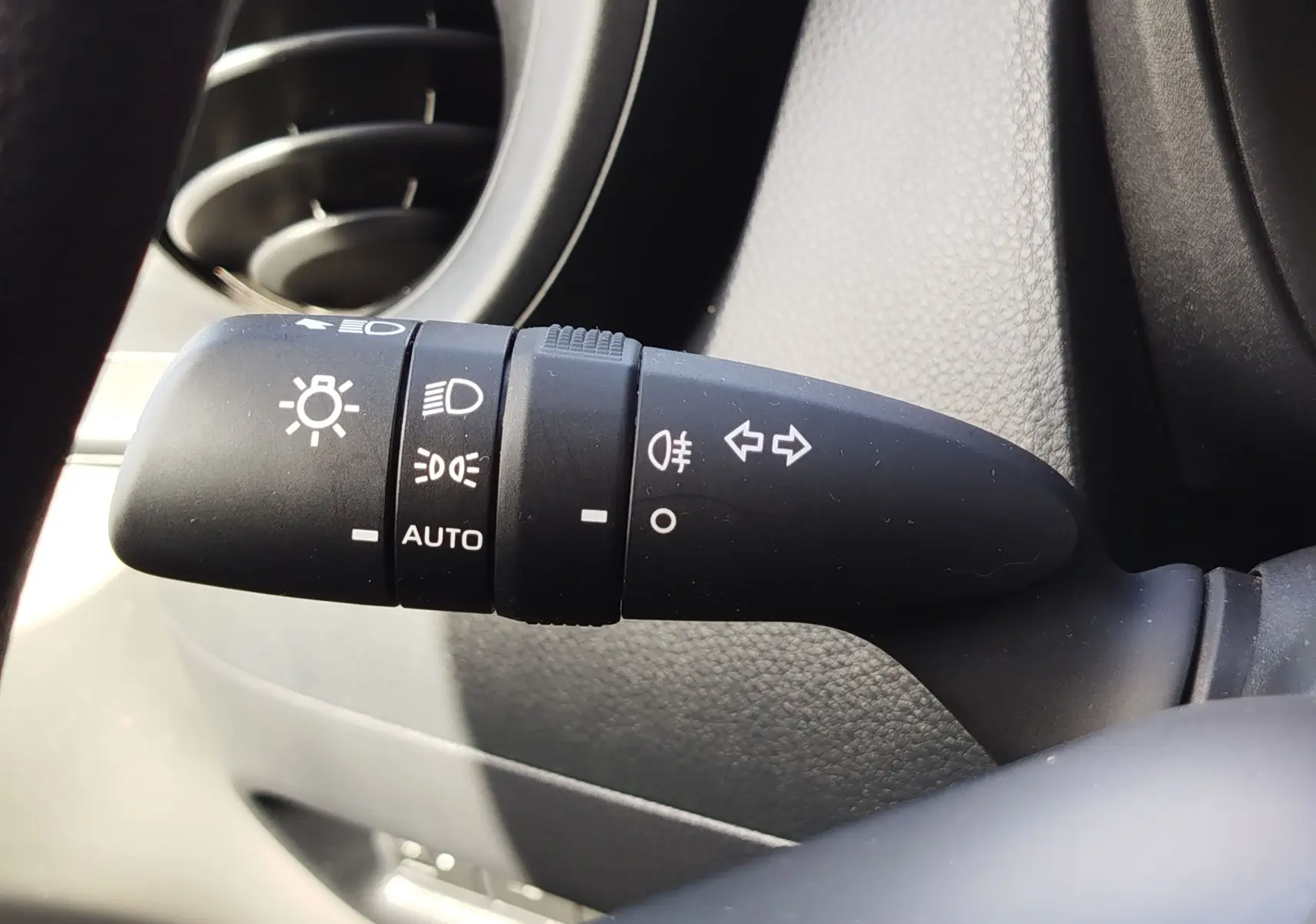 Gros plan sur la commande des feux et clignotants noire dans l'habitacle d'une Toyota Aygo X blanche.