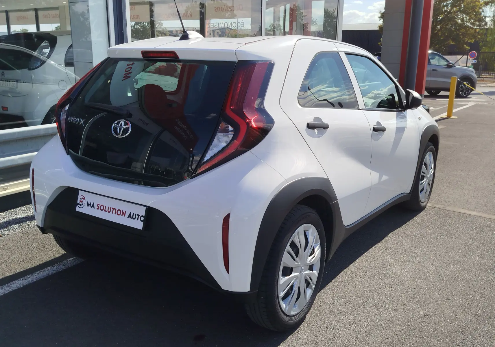 Toyota Aygo X blanc pur vue 3/4 arrière droit, avec feux arrière en forme de boomerang et jantes alliage.