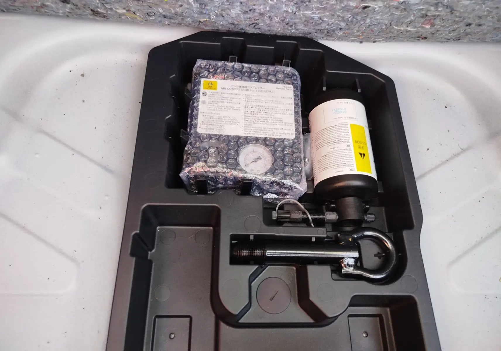Kit de réparation pneu avec compresseur et produit d'étanchéité dans le coffre d'une Toyota Aygo X blanche.