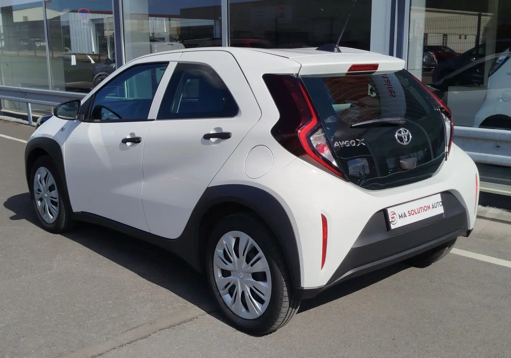 Toyota Aygo X blanche vue 3/4 arrière droit, avec hayon noir contrastant et feux arrière en forme de C.