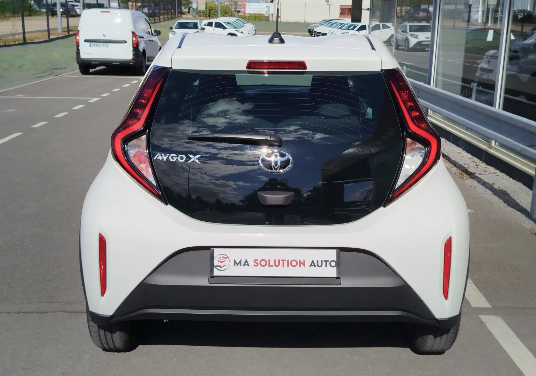 Vue arrière d'une Toyota Aygo X blanche Pure 2023 avec hayon noir brillant et feux arrière en forme de boomerang.