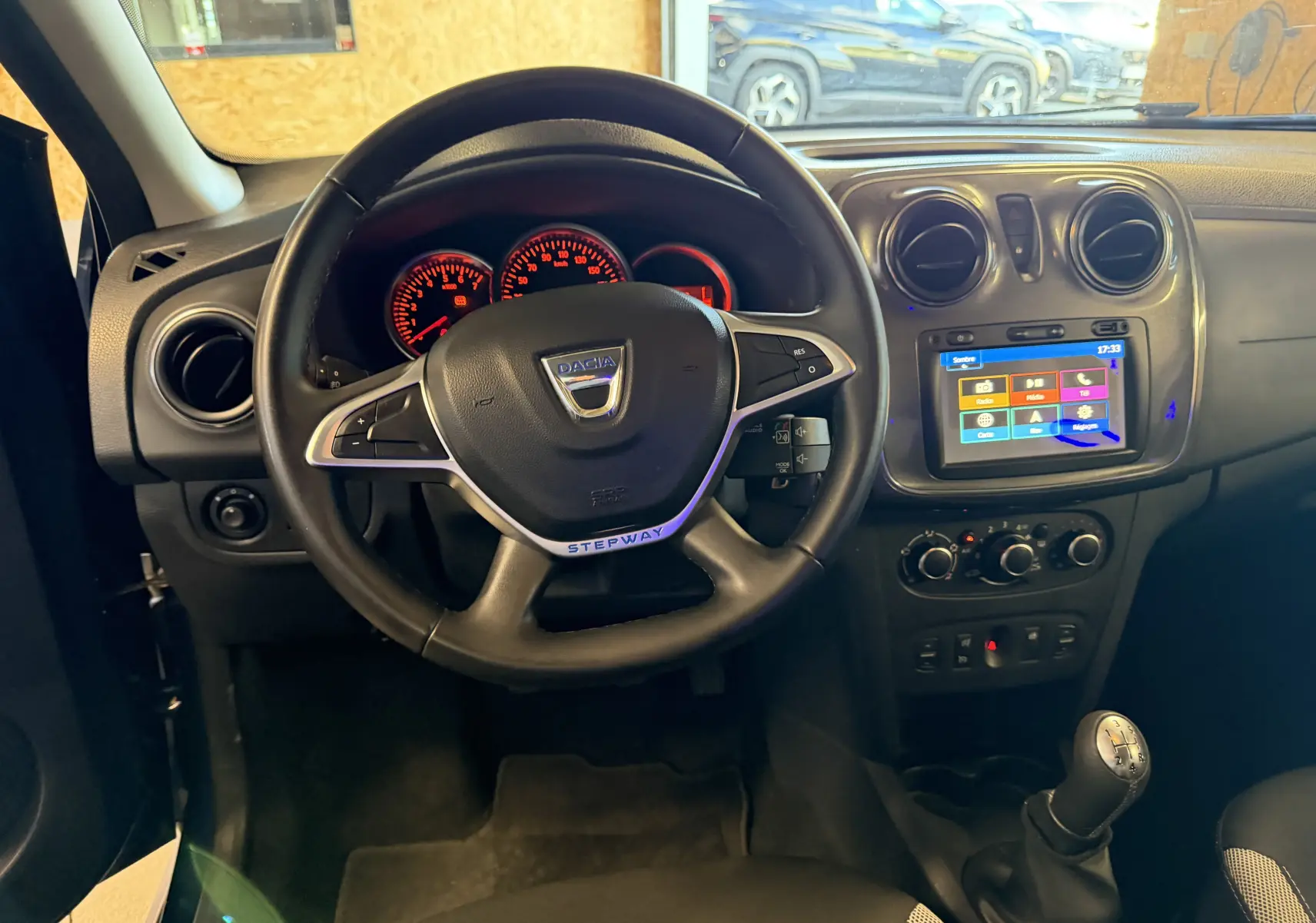 Vue intérieure centrée sur le volant noir de la Dacia Sandero Stepway bleu, avec tableau de bord et écran tactile visibles.