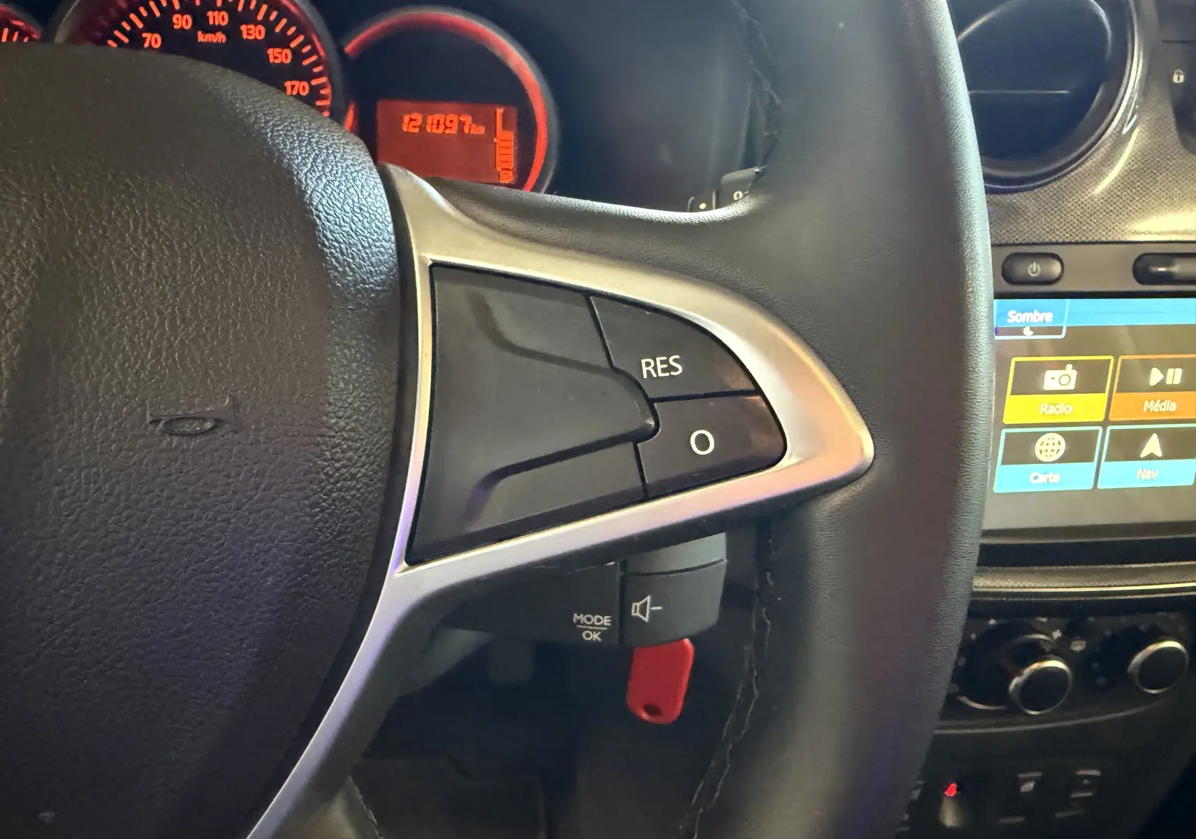 Gros plan sur le volant noir de la Dacia Sandero Stepway 2019 avec commandes au volant et tableau de bord éclairé rouge.