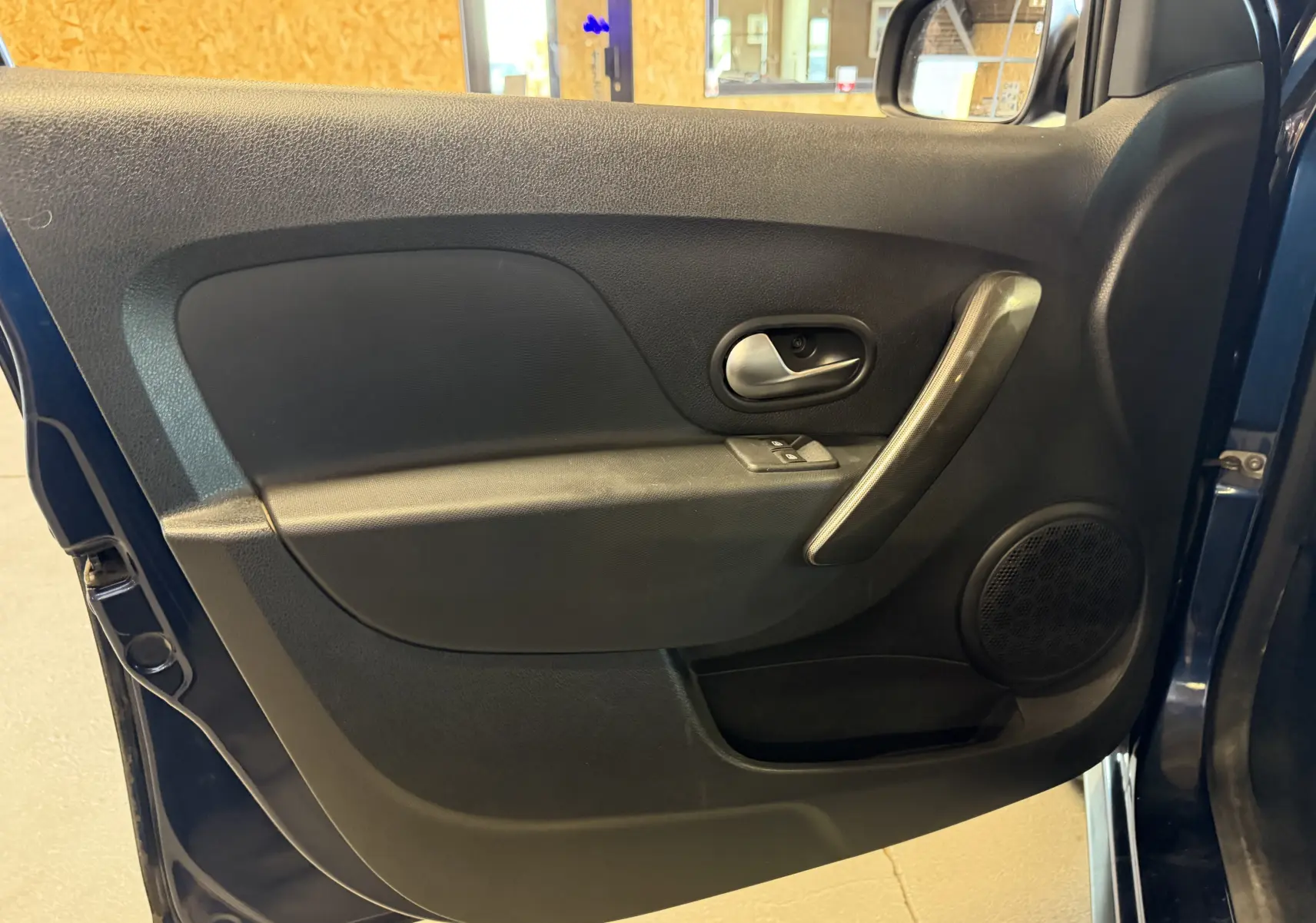 Vue intérieure de la porte avant gauche bleu foncé de la Dacia Sandero Stepway 2019 avec poignée argentée et commande de vitre.