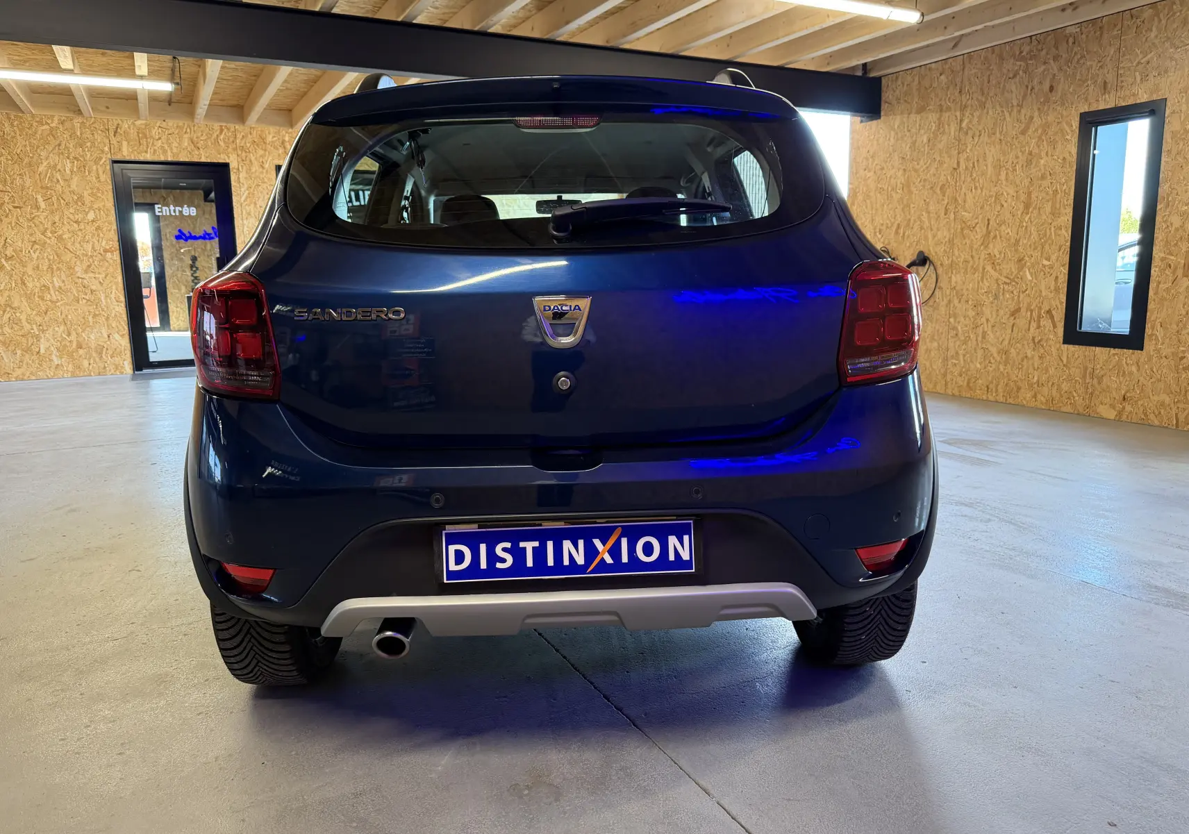 Vue arrière d'une Dacia Sandero Stepway bleu foncé 2019, avec logo et plaque Distinxion visibles en intérieur.