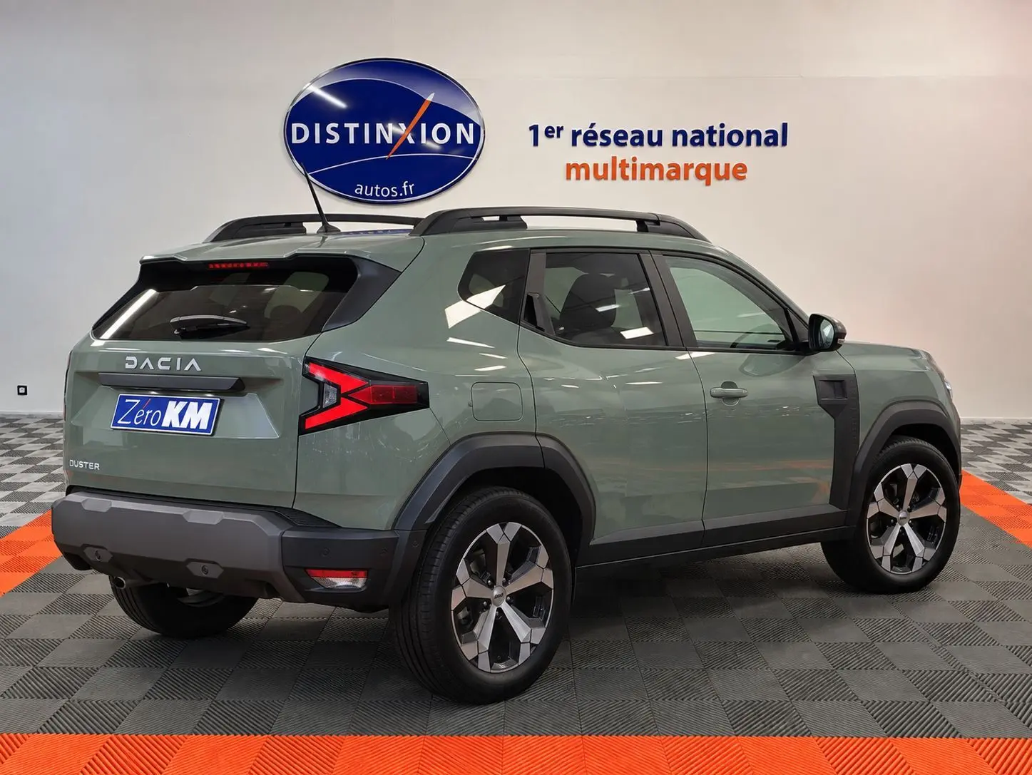 Vue 3/4 arrière droite du Dacia Duster 2026 vert cèdre avec jantes alliage et barres de toit noires.