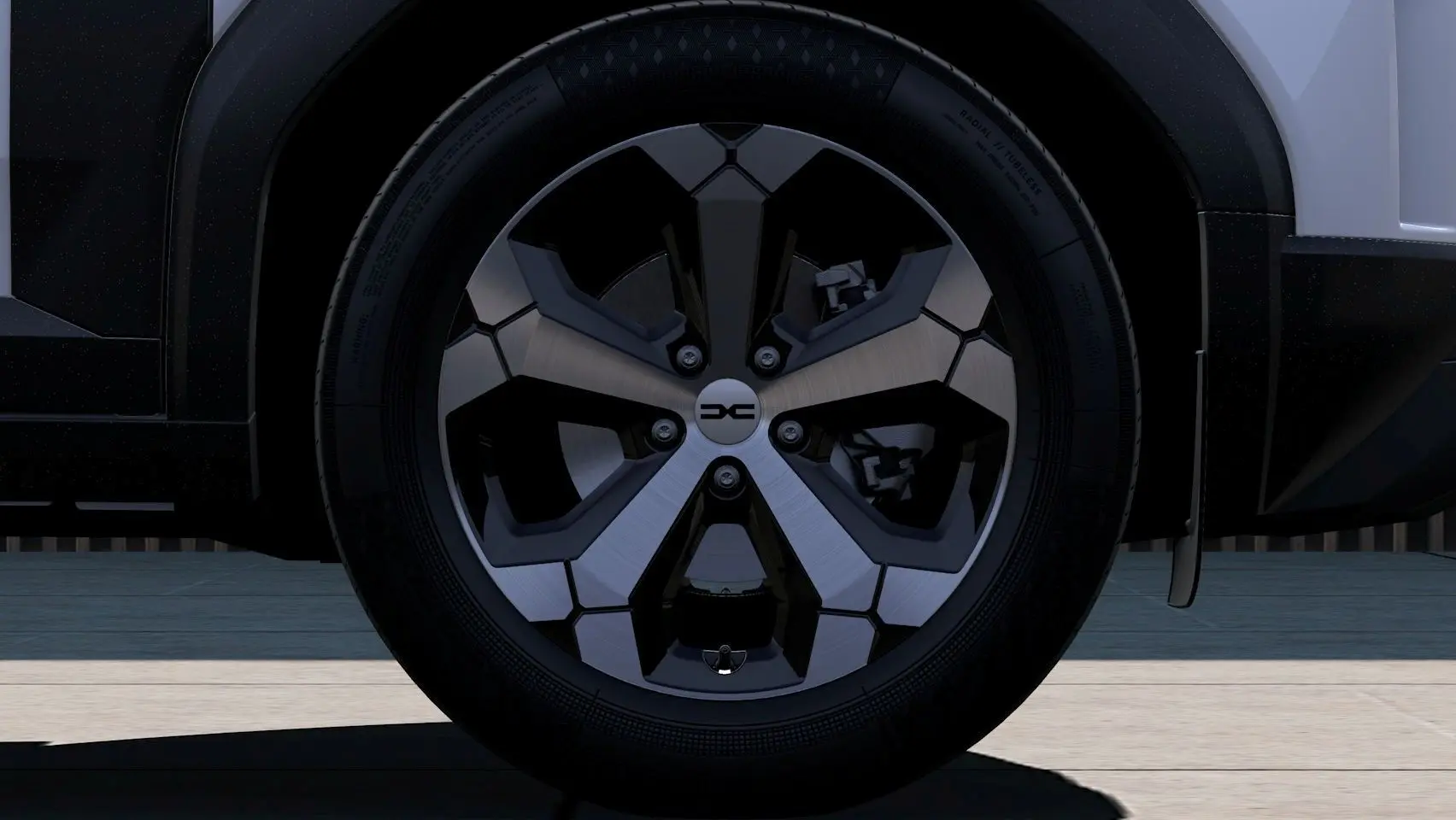 Gros plan sur la roue avant droite du Dacia Duster 2026, jante alliage noire et argentée, partie basse du véhicule blanche visible.