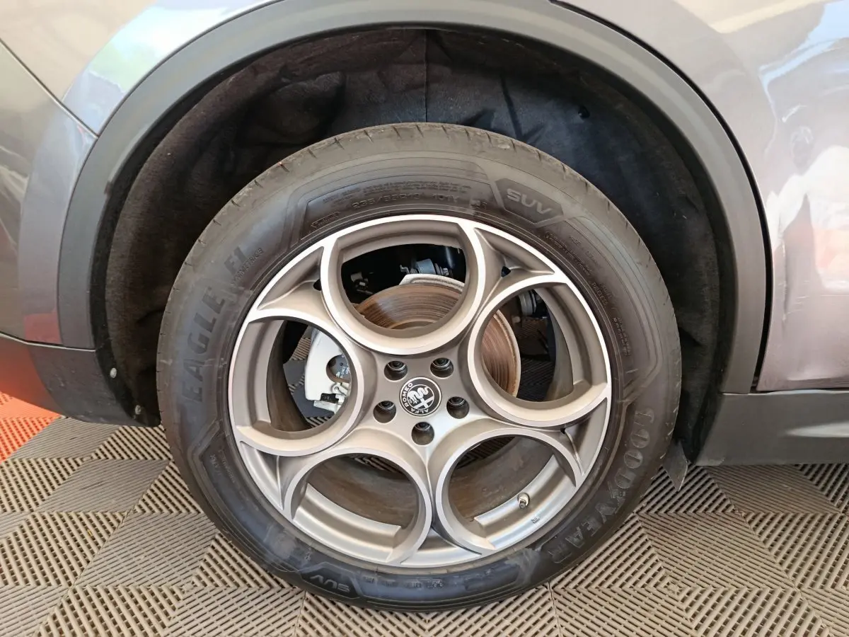 Gros plan sur la roue avant gauche gris foncé d’un Alfa Romeo Stelvio 2024 avec jante en alliage à cinq cercles entrelacés.