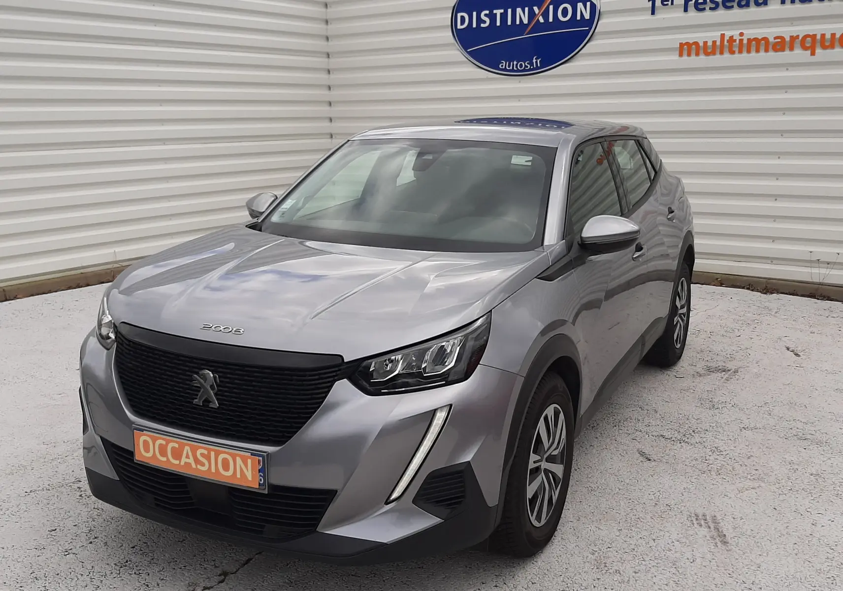 Peugeot 2008 gris Artense vue 3/4 avant droit, avec calandre noire et phares LED, stationnée devant un mur blanc.