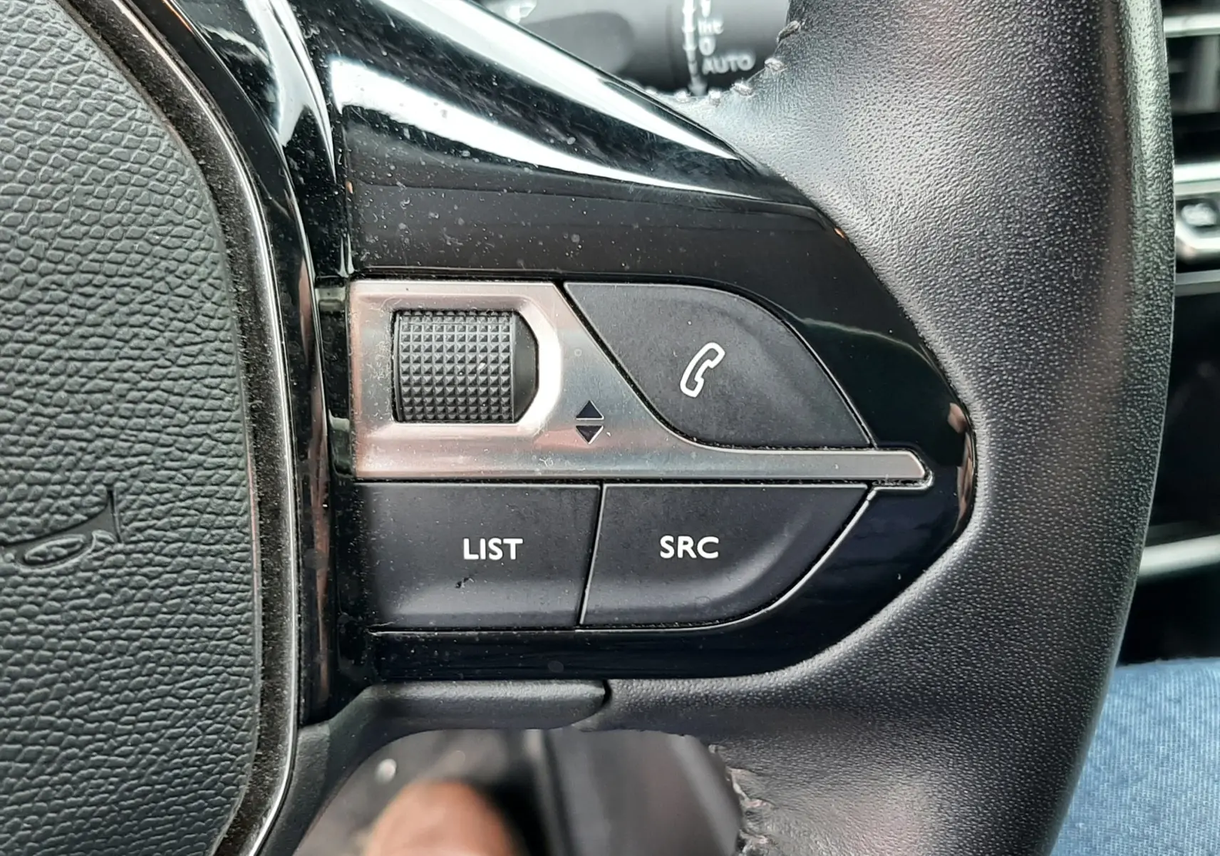 Gros plan sur les commandes au volant côté gauche du Peugeot 2008 gris Artense, avec boutons LIST, SRC et téléphone.