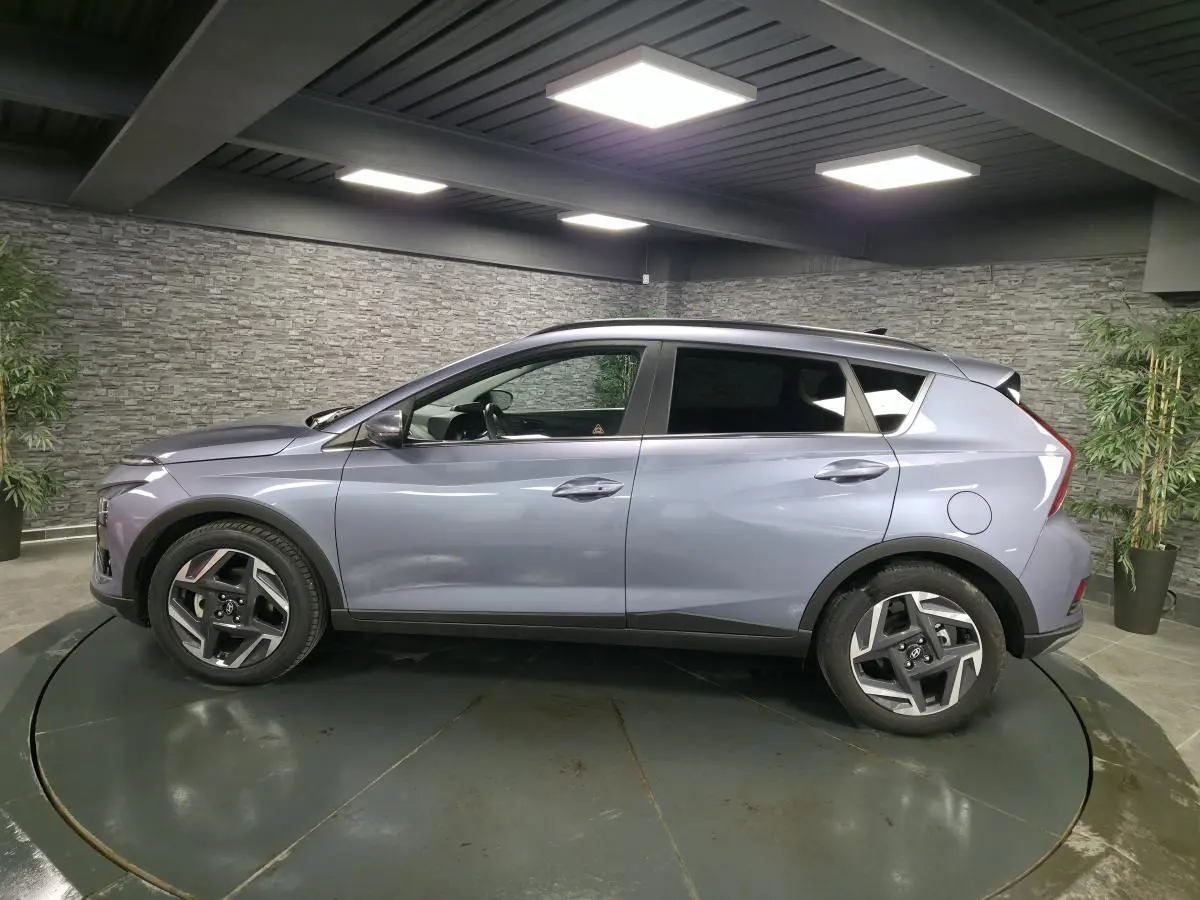 Vue de profil côté gauche d’un Hyundai Bayon gris métallisé avec jantes alliage 17 pouces dans un showroom.