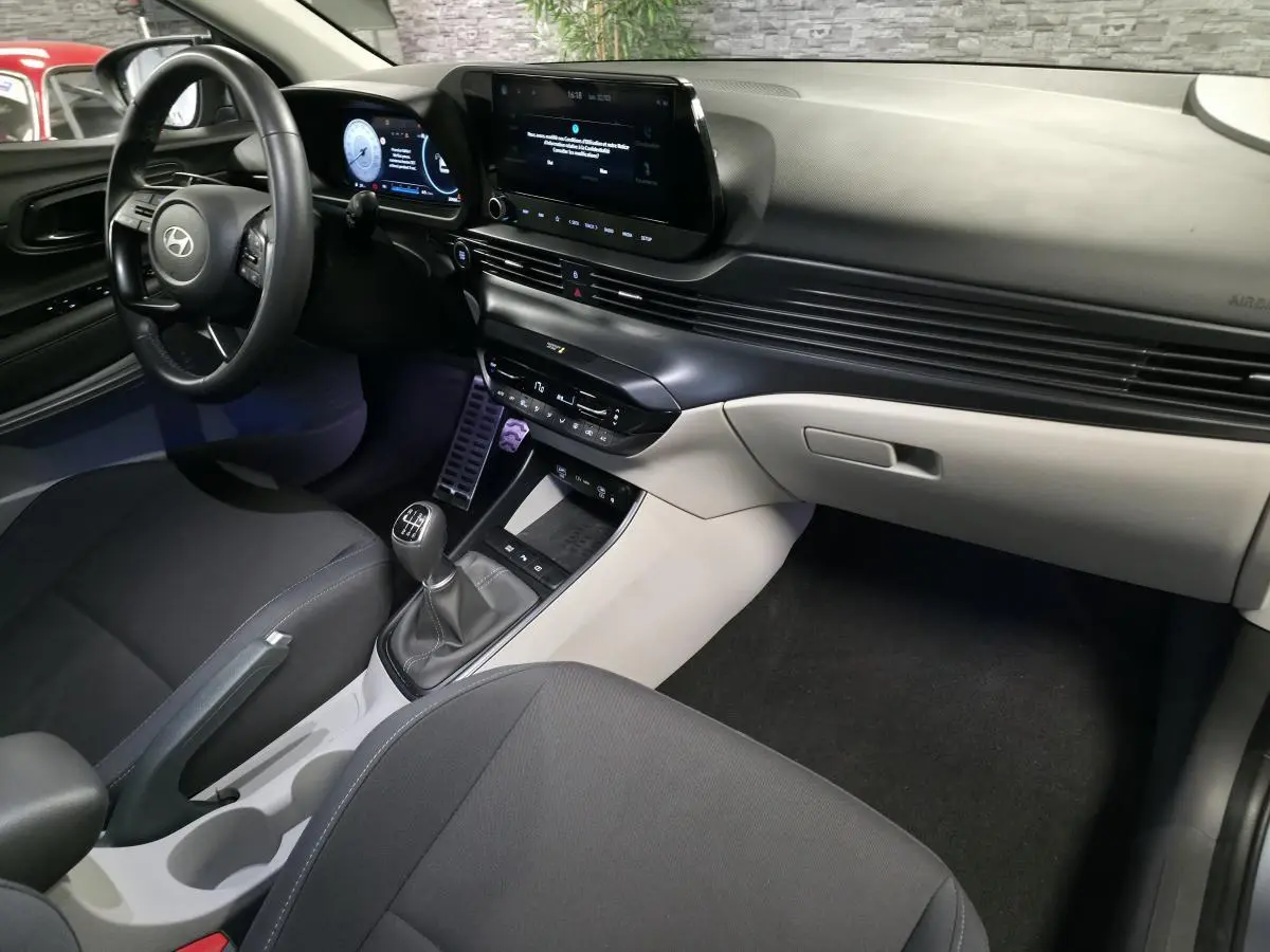 Vue intérieure côté conducteur du Hyundai Bayon 2025, tableau de bord bi-ton gris et noir avec écran tactile et levier de vitesses manuel.