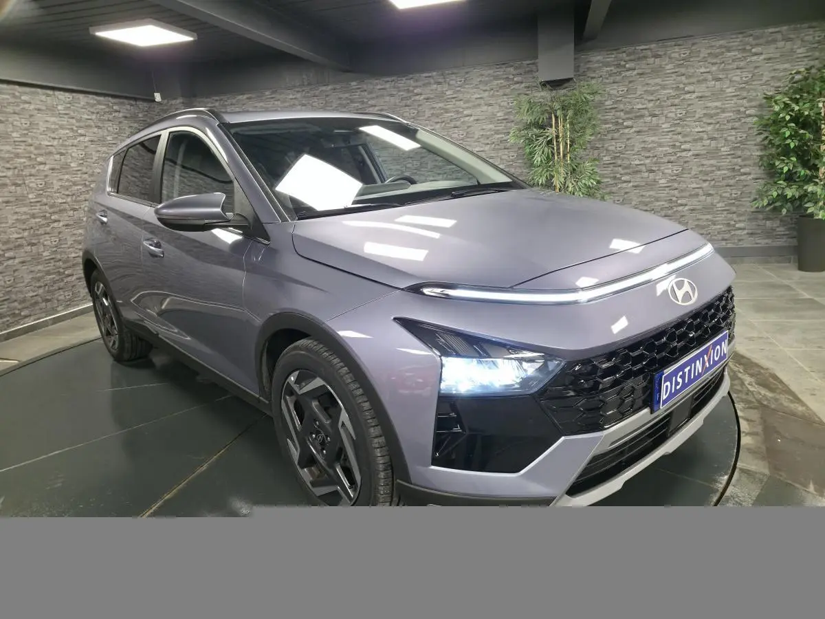 Hyundai Bayon gris métallisé vue 3/4 avant droit avec calandre noire laquée et feux LED allumés.