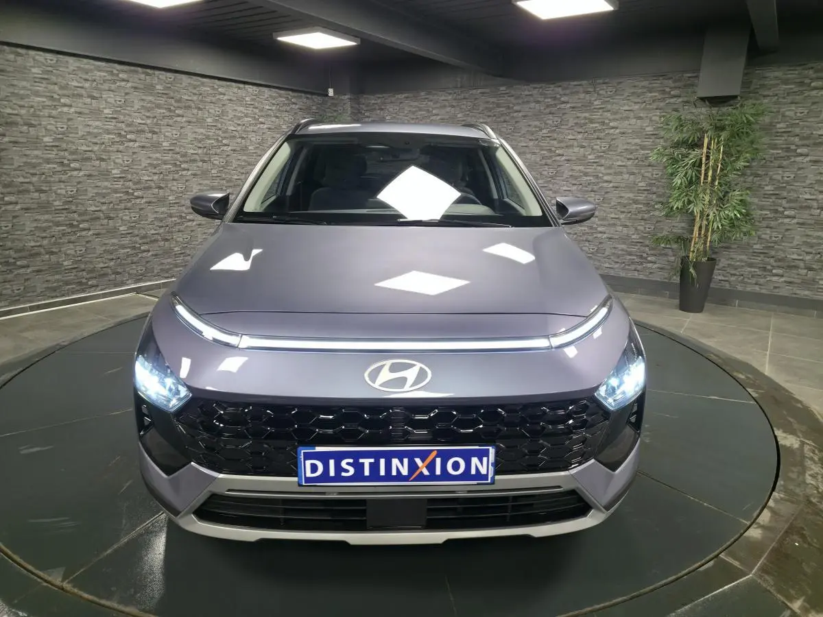 Vue avant d'une Hyundai Bayon gris métallisé avec calandre noire laquée et feux LED allumés dans un showroom.