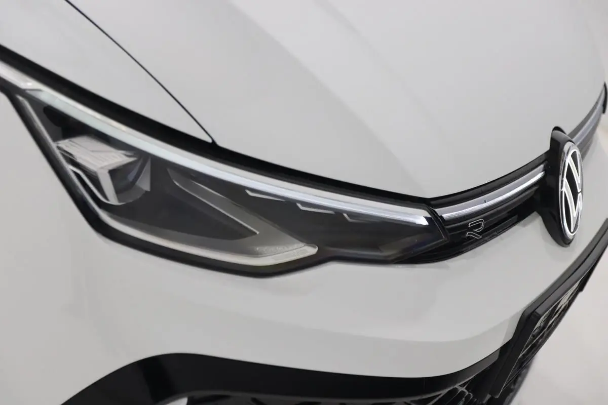 Gros plan sur le phare avant gauche blanc d’une Volkswagen Golf 2.0 TDI R-Line avec logo VW et bande LED.