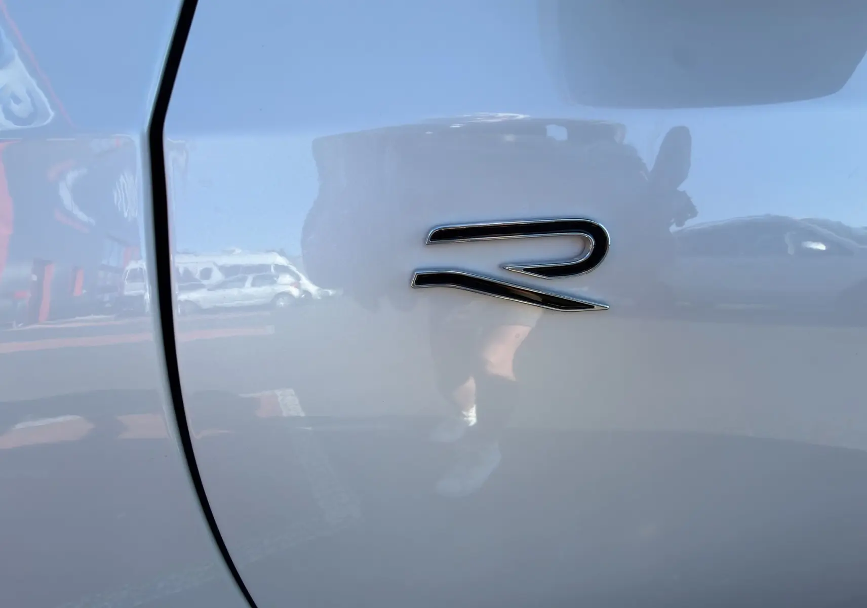 Gros plan sur l'emblème "R" noir brillant sur la carrosserie blanche d'une Volkswagen Golf 2.0 TDI R-Line.