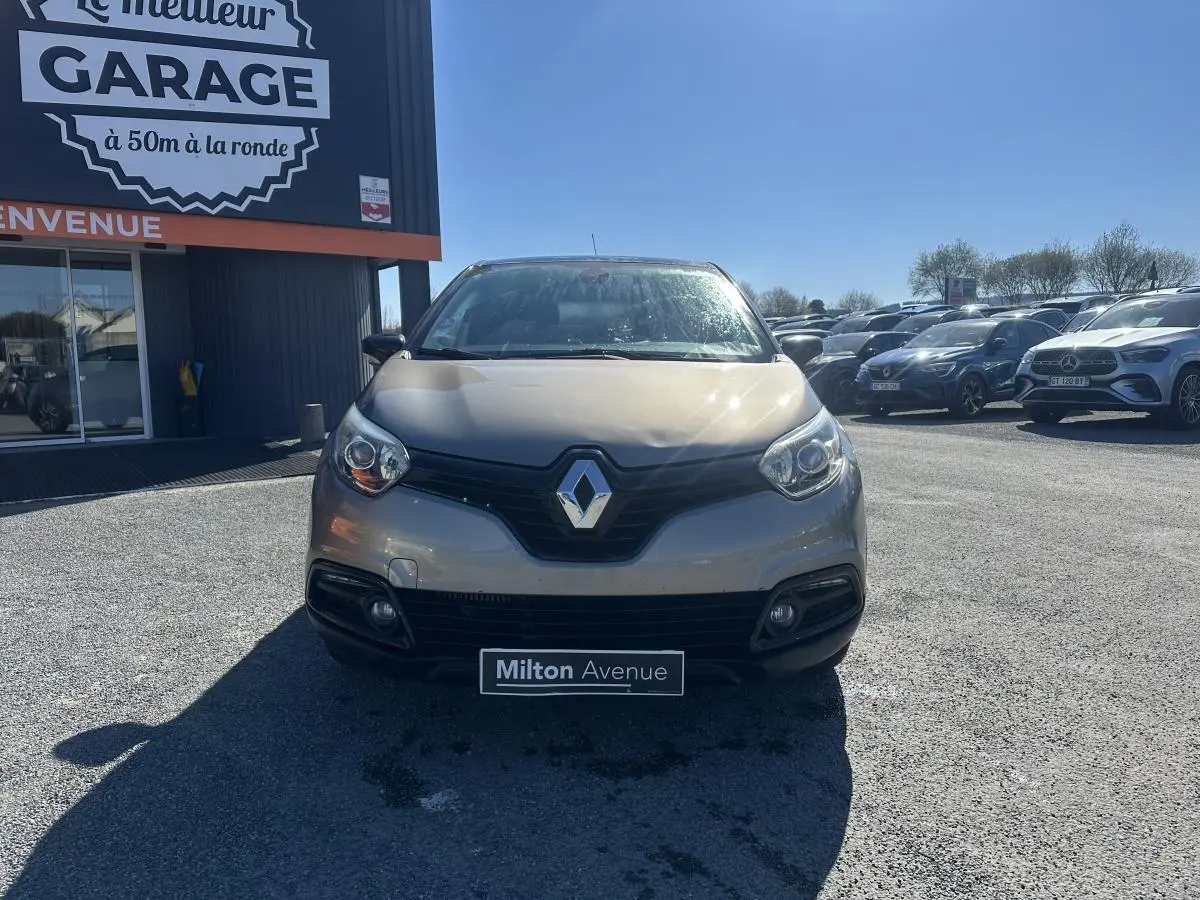 Vue avant d'un Renault Captur beige métallisé 2014, avec calandre noire et phares arrondis sous un ciel dégagé.