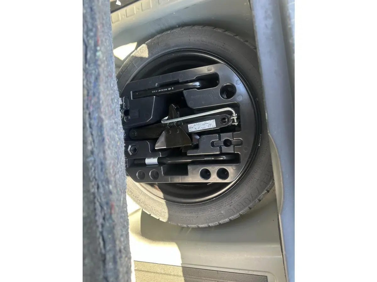 Vue rapprochée de la roue de secours galette et outils dans le coffre d’un Renault Captur beige 2014.