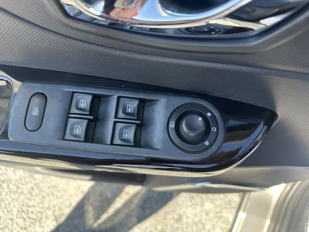 Gros plan sur les commandes de lève-vitres et réglage des rétroviseurs côté conducteur du Renault Captur beige.