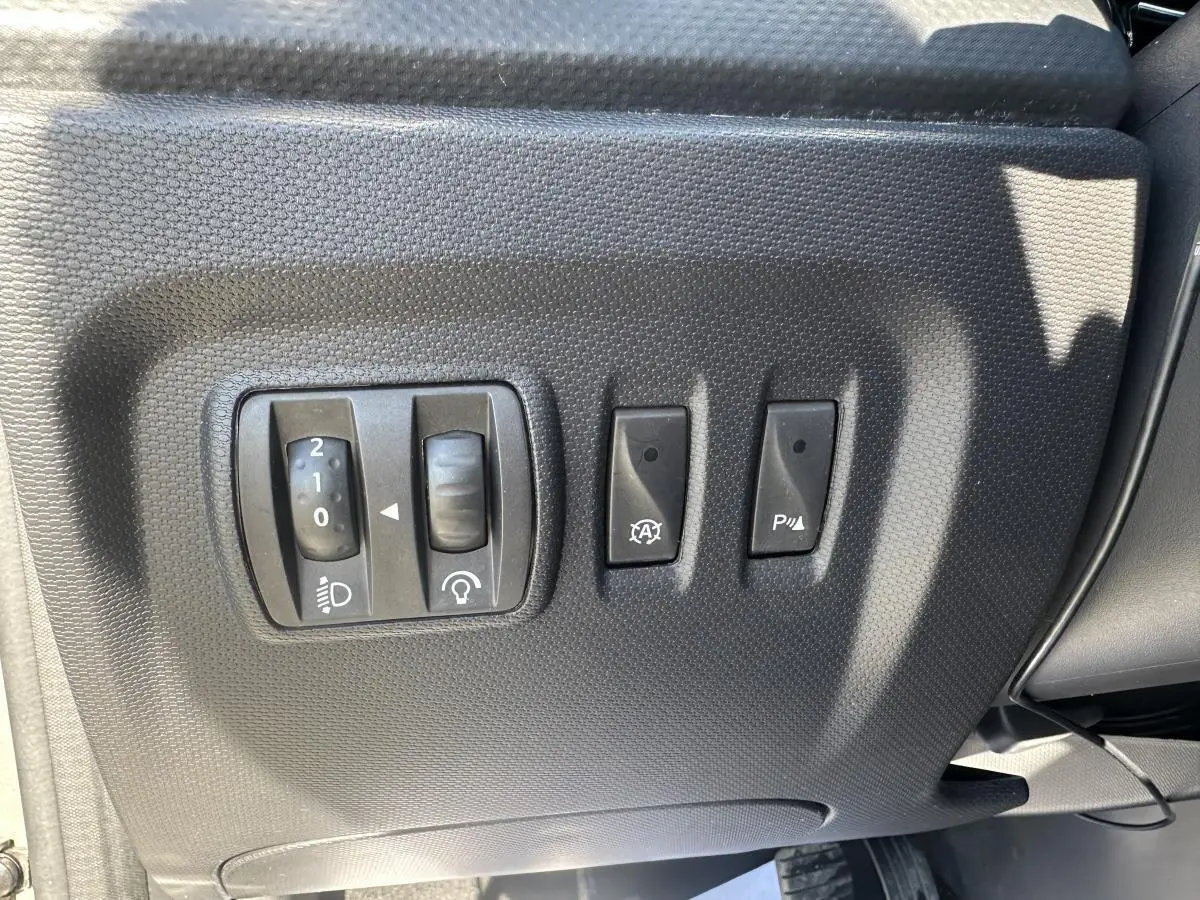Gros plan sur les commandes de réglage des phares et aides à la conduite côté conducteur du Renault Captur beige 2014.