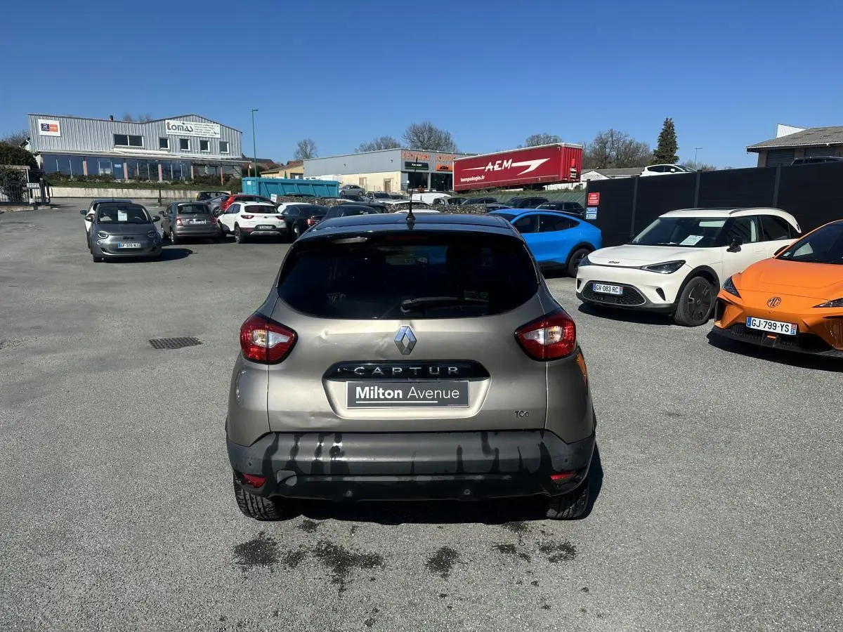 Vue arrière d'un Renault Captur beige métallisé 2014 avec toit noir, stationné sur un parking ensoleillé.