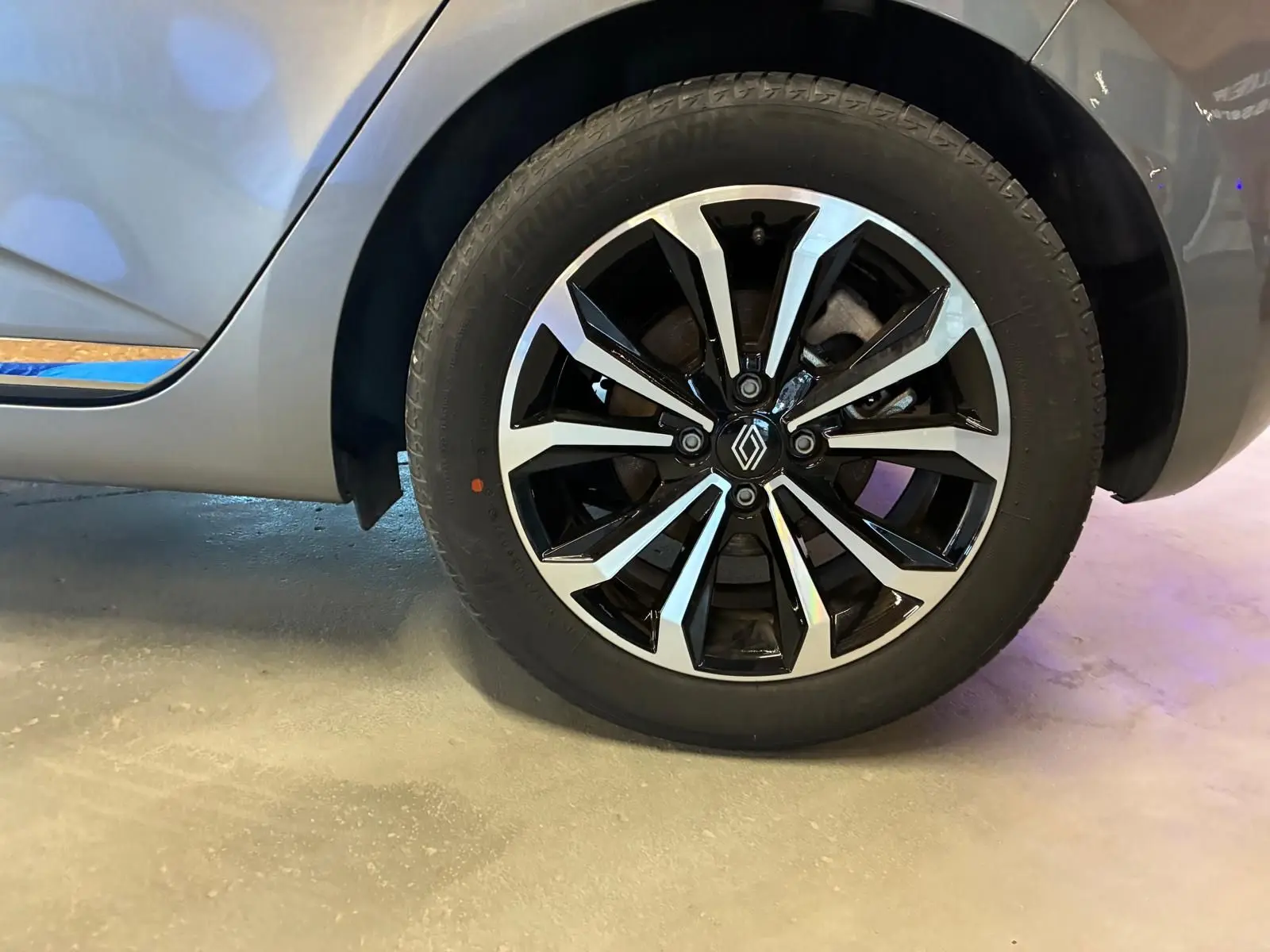 Gros plan sur la roue avant droite de la Renault Clio gris schiste 2025 avec jante alliage bicolore et logo Renault central.